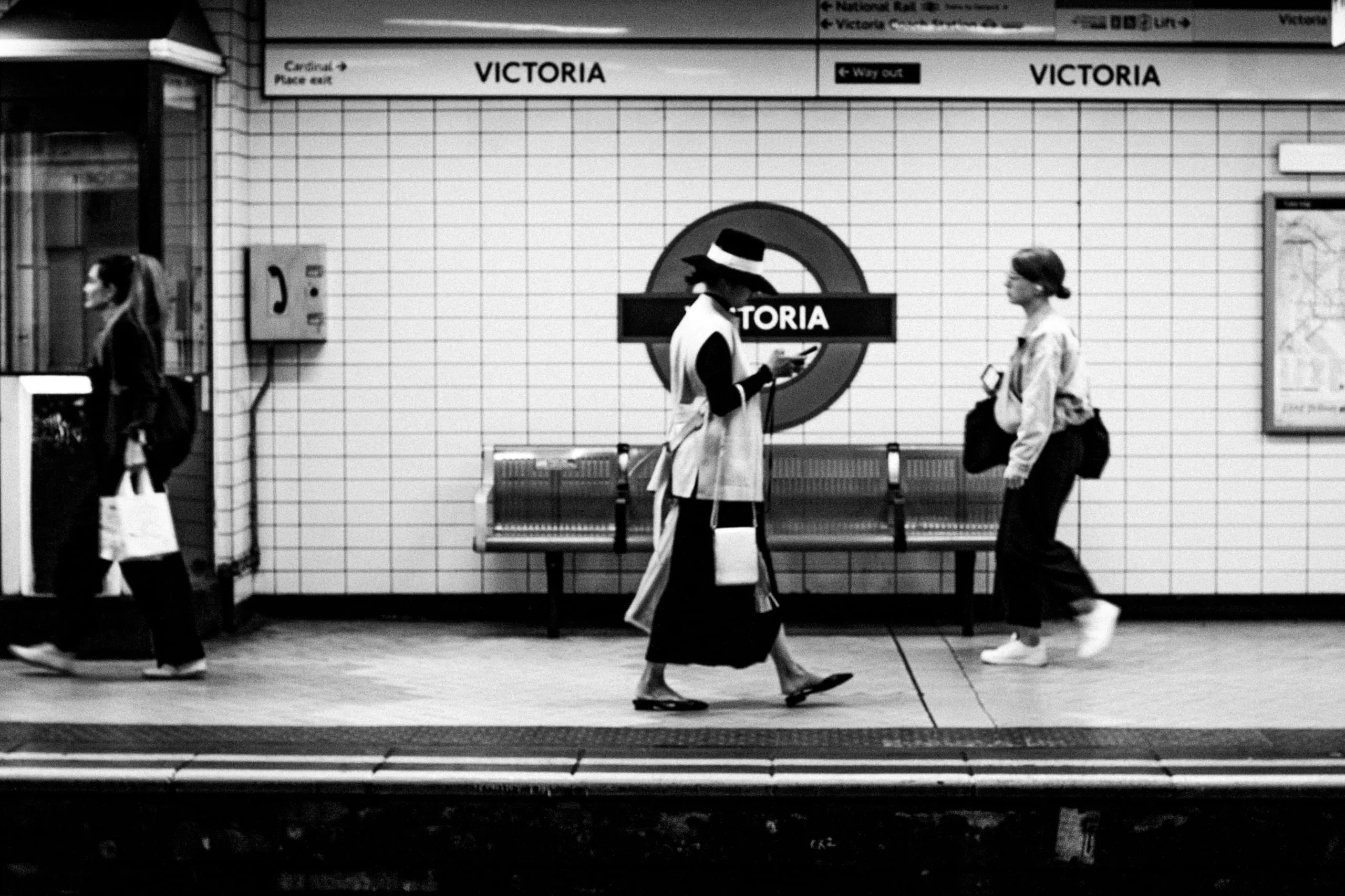 A woman walks along the platform past the roundel, Victoria Underground station