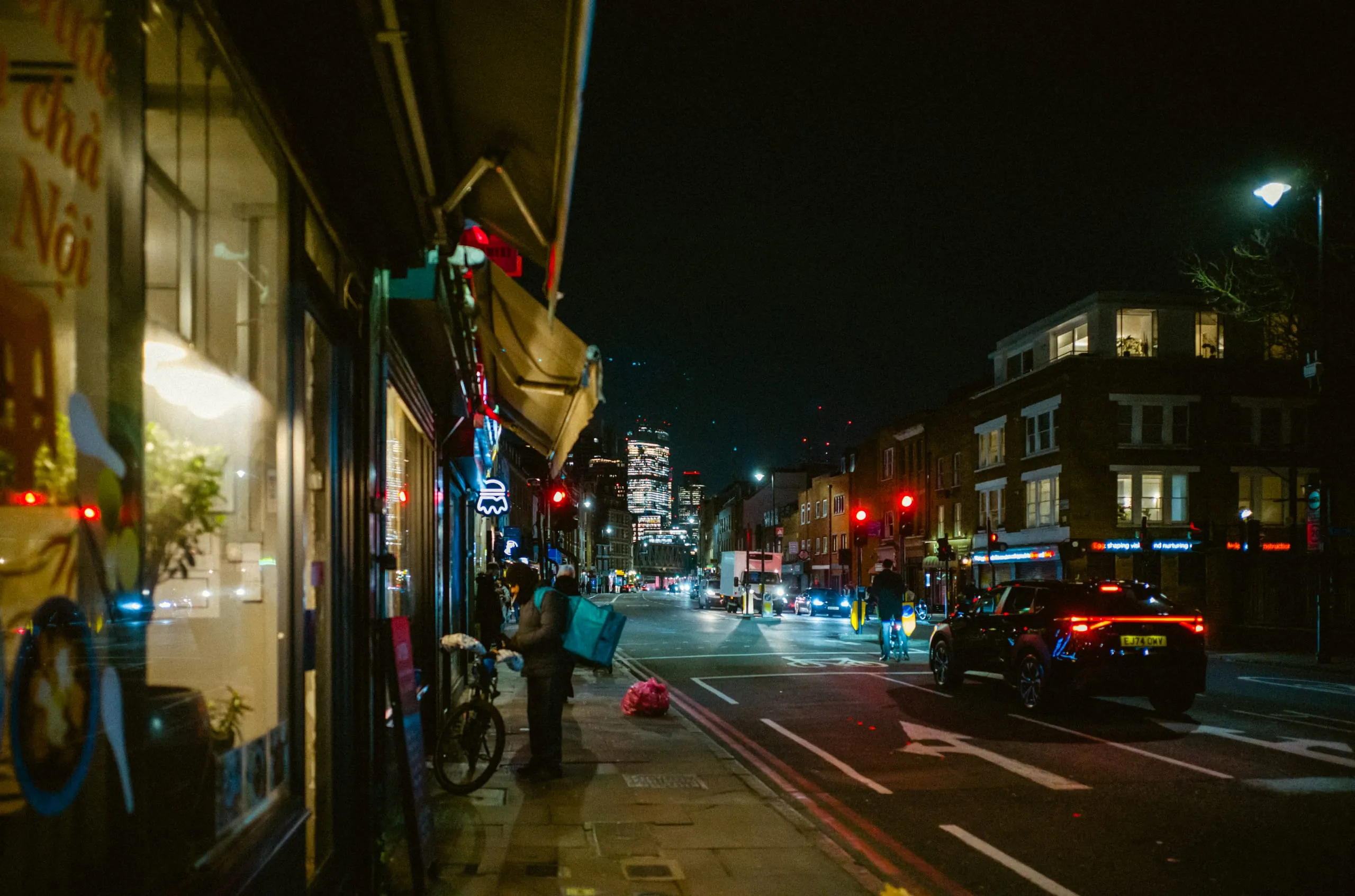 A delivery rider stands on a street at night, London