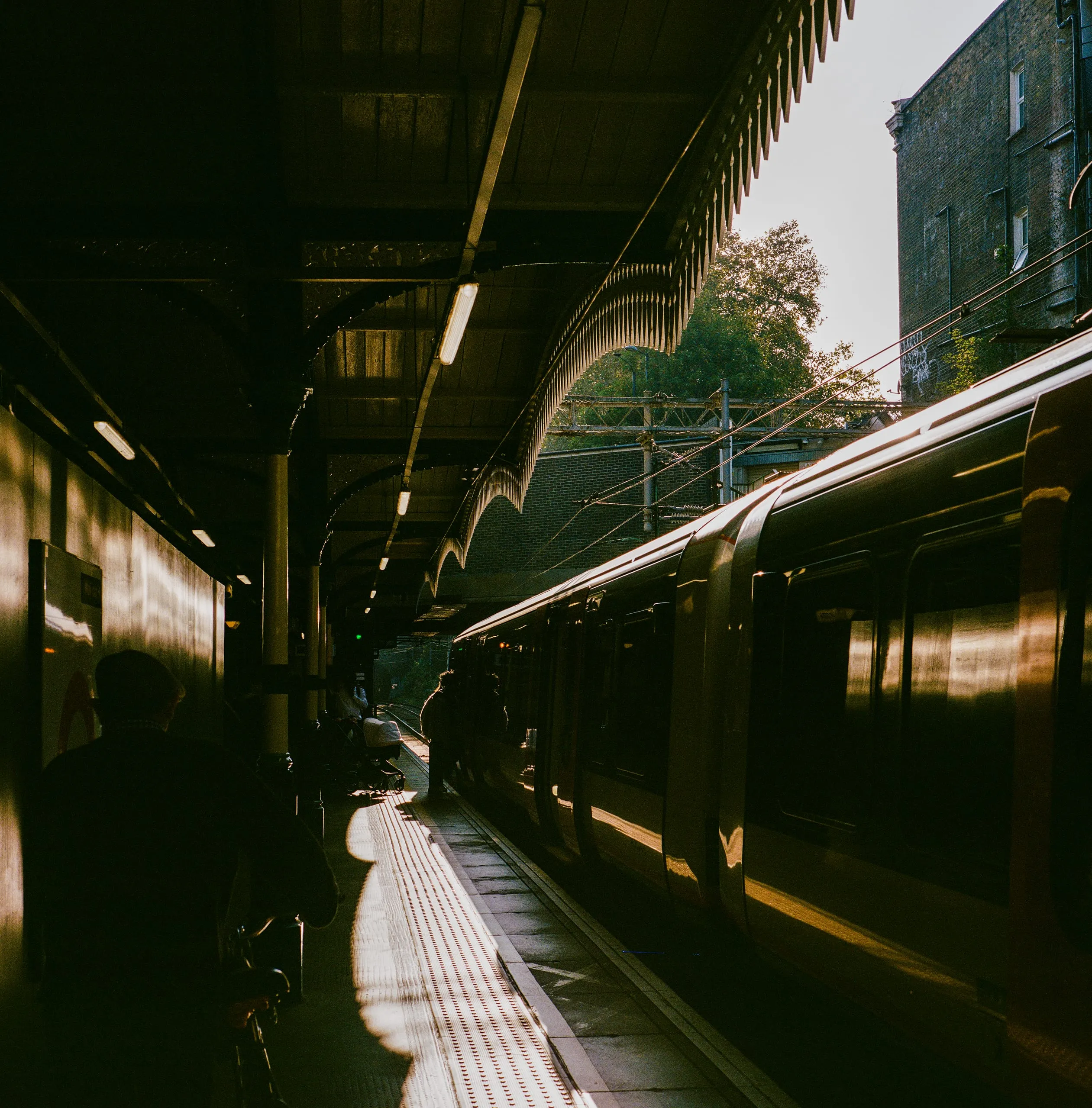 An overground train pulls into Clapton station platform in low afternoon sun