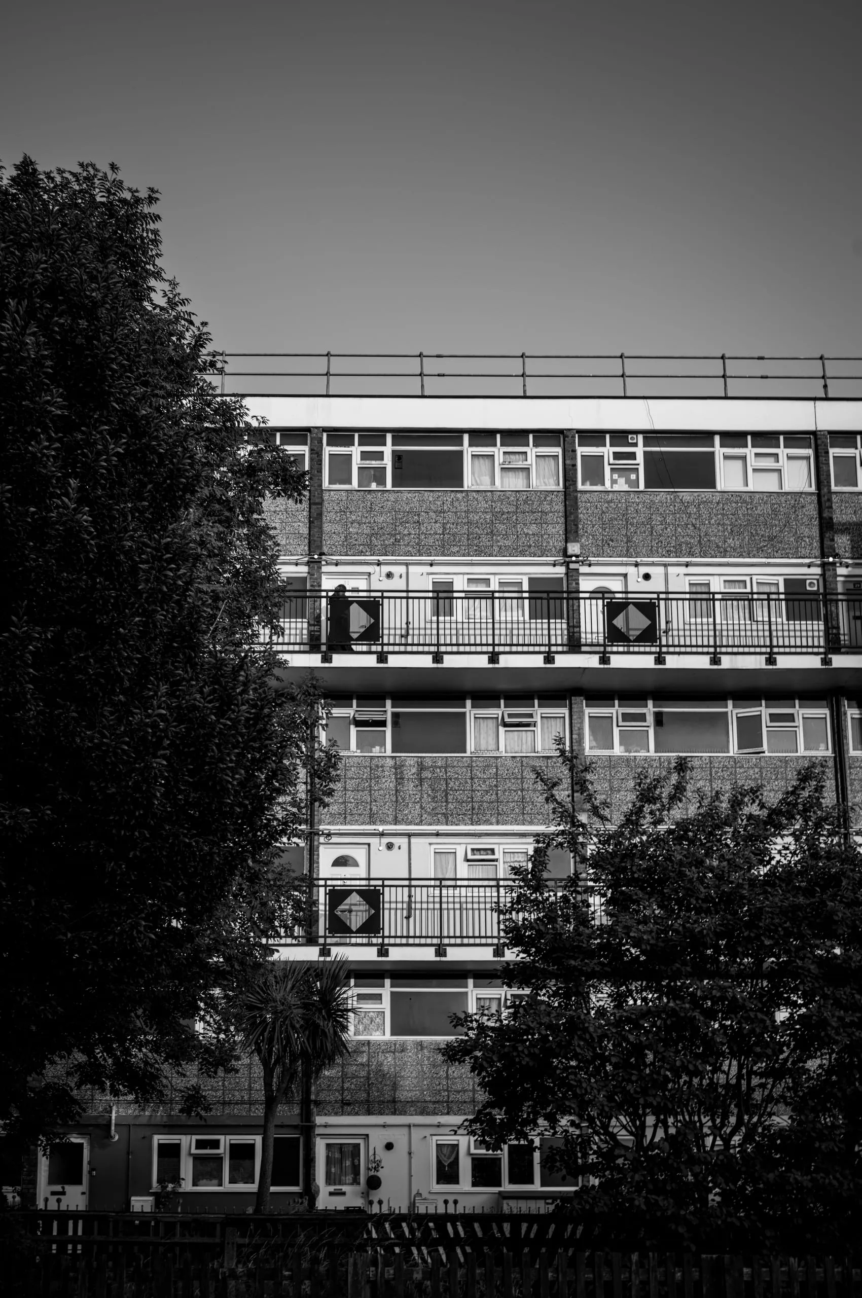 A woman stands in front of a block of council housing flats, Leyton