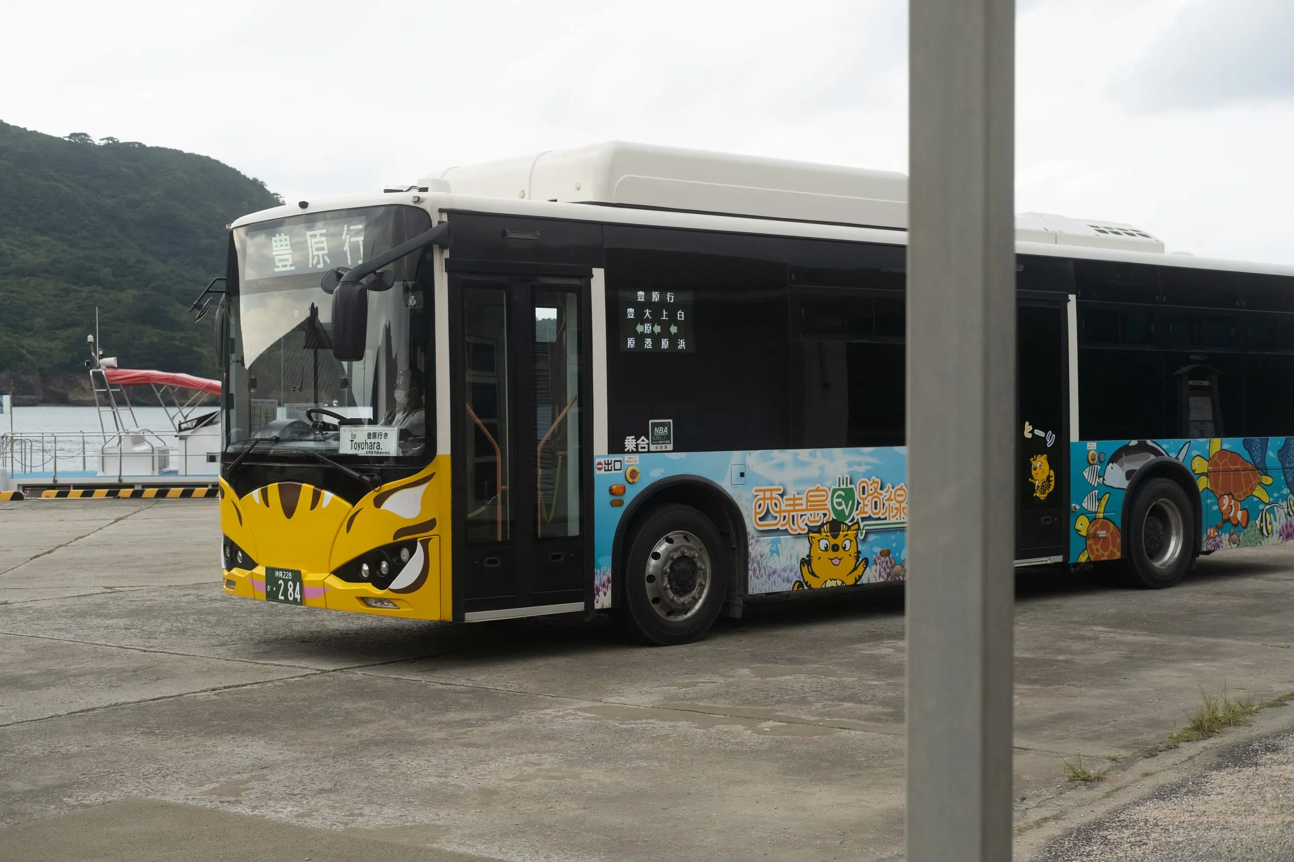 A single-decker iriomote cat bus parked at a harbourside terminal