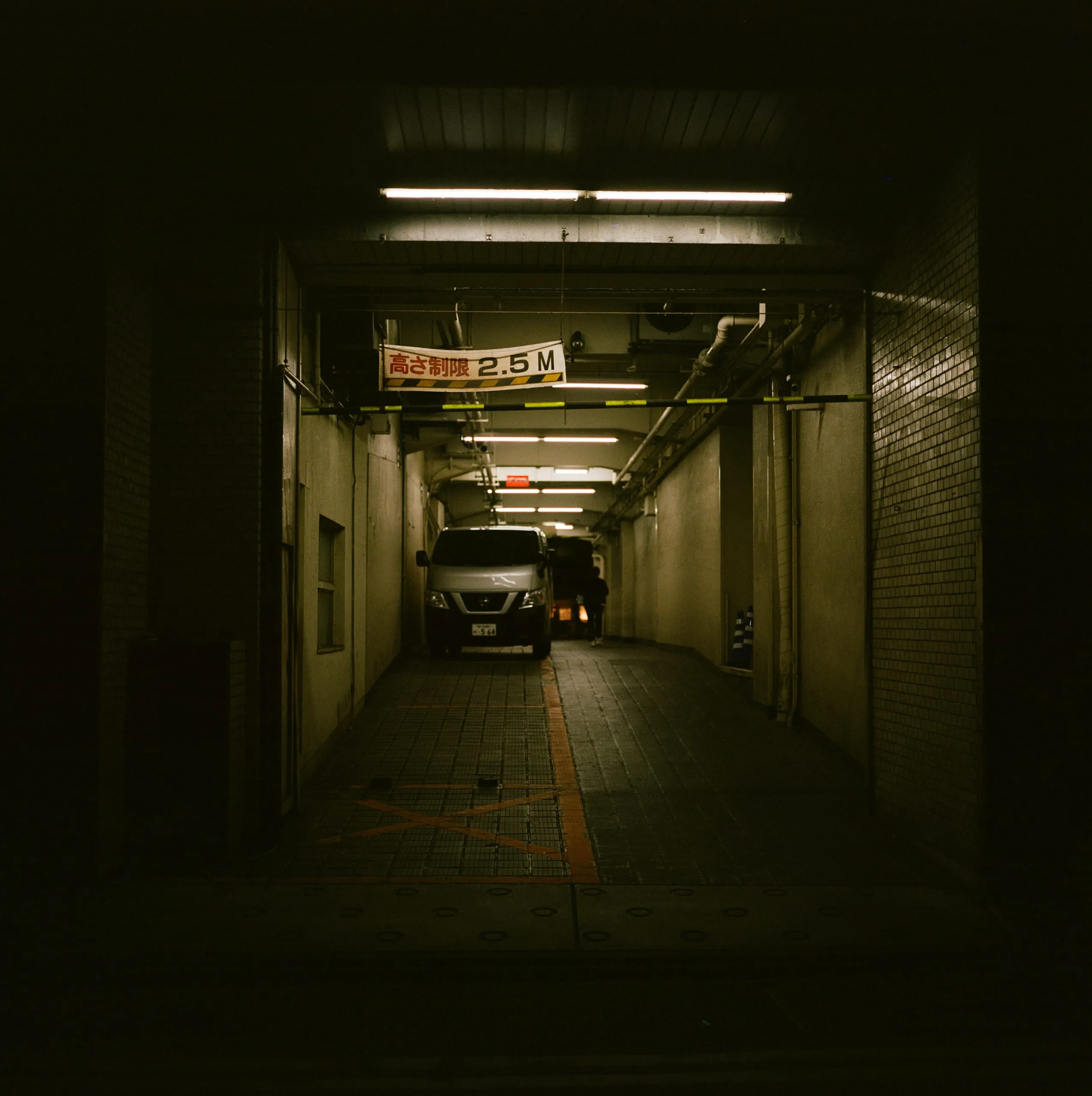 A van parked under a low-clearance sign in a dim alley
