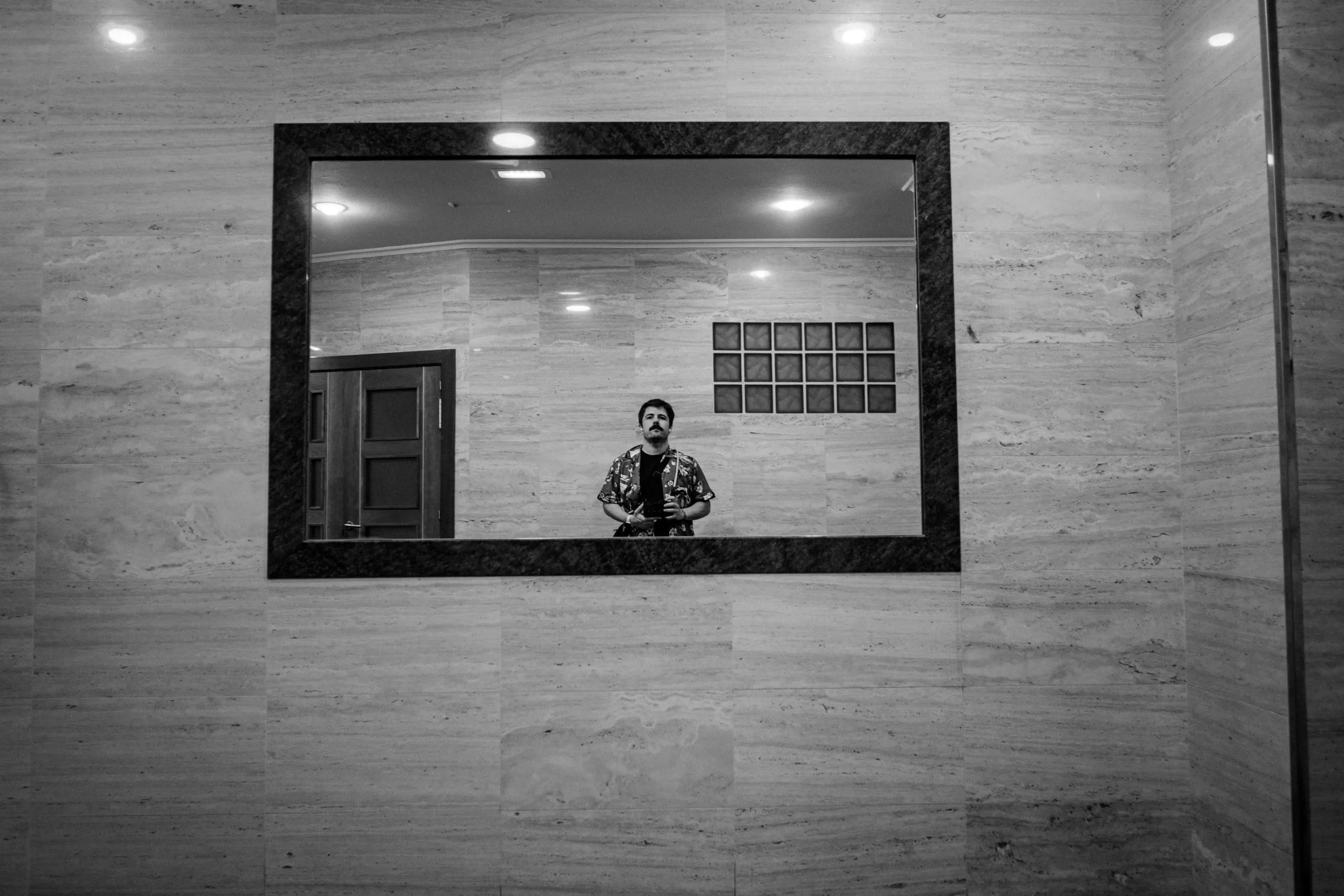 A man reflected in a framed mirror on a marble wall