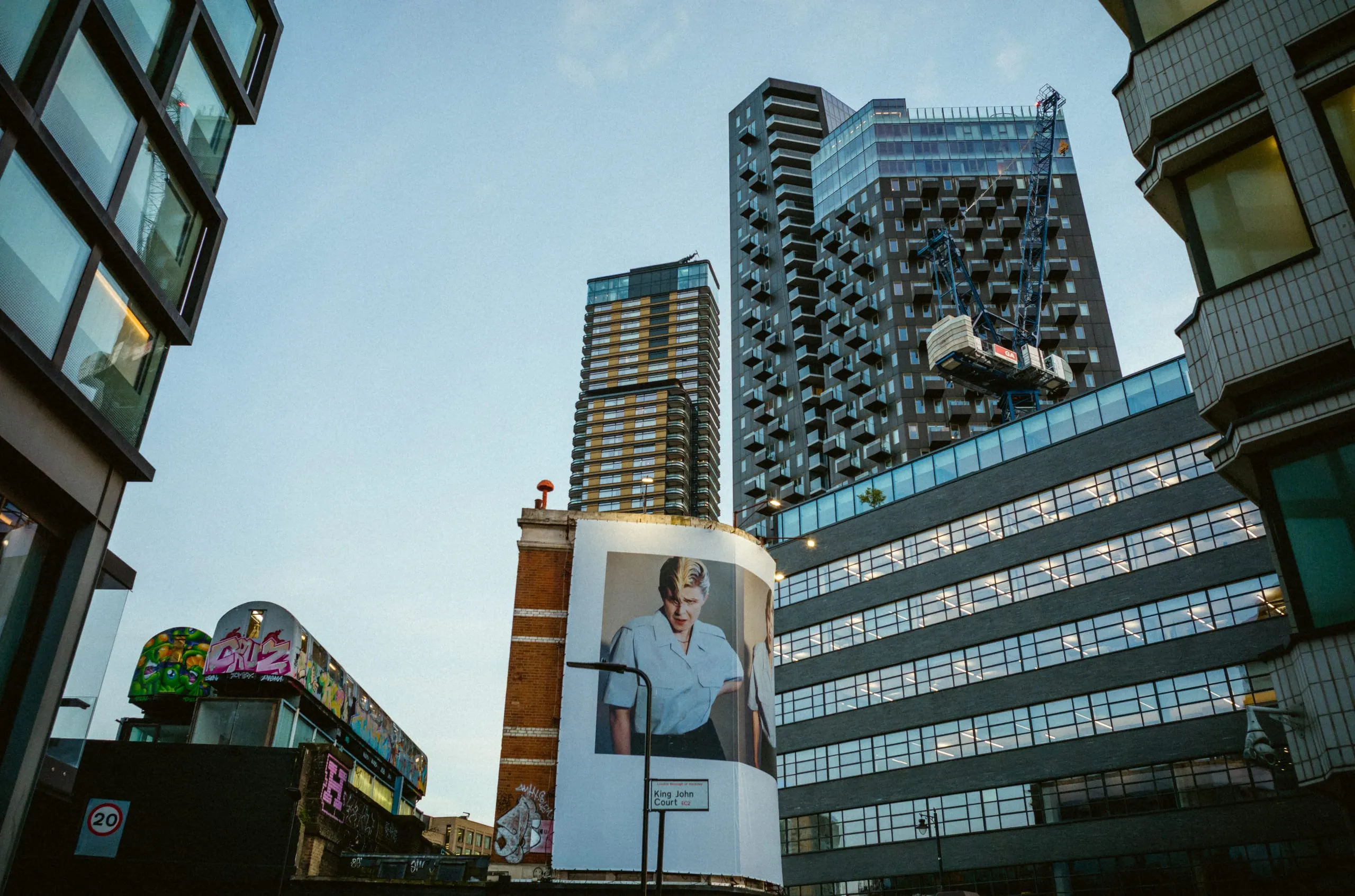 A large portrait on a building below tower blocks and a construction crane at dusk, Stratford