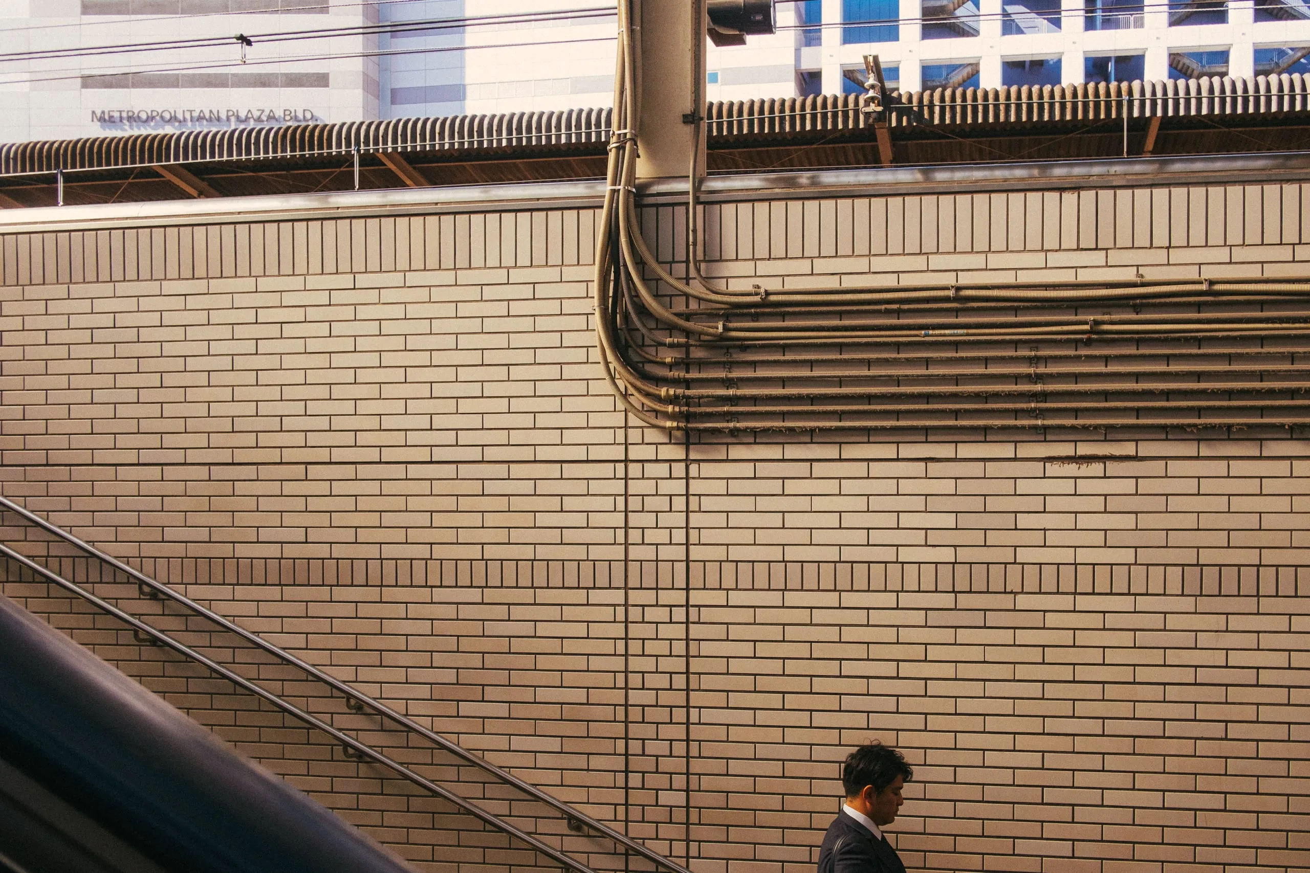 A man walks past a tiled station wall hung with cables