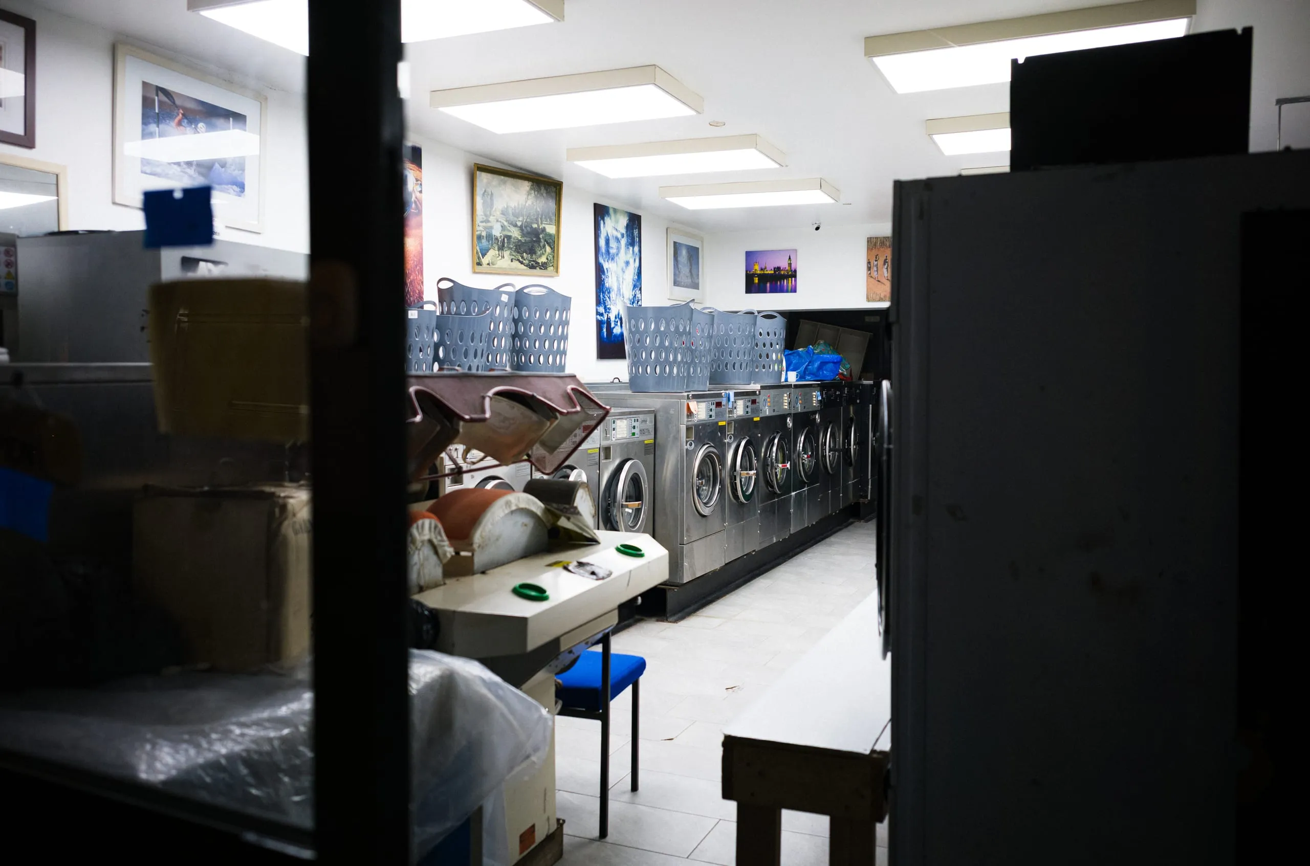The interior of a launderette with rows of washing machines and laundry baskets