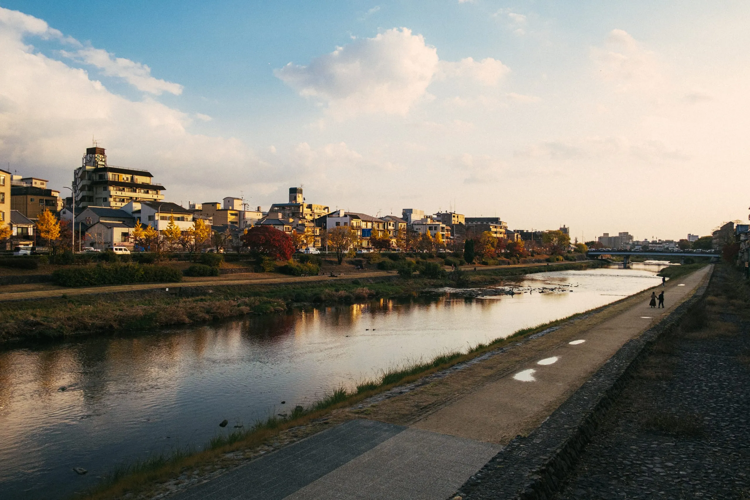 A couple walks along the river embankment at dusk in Kamogawa