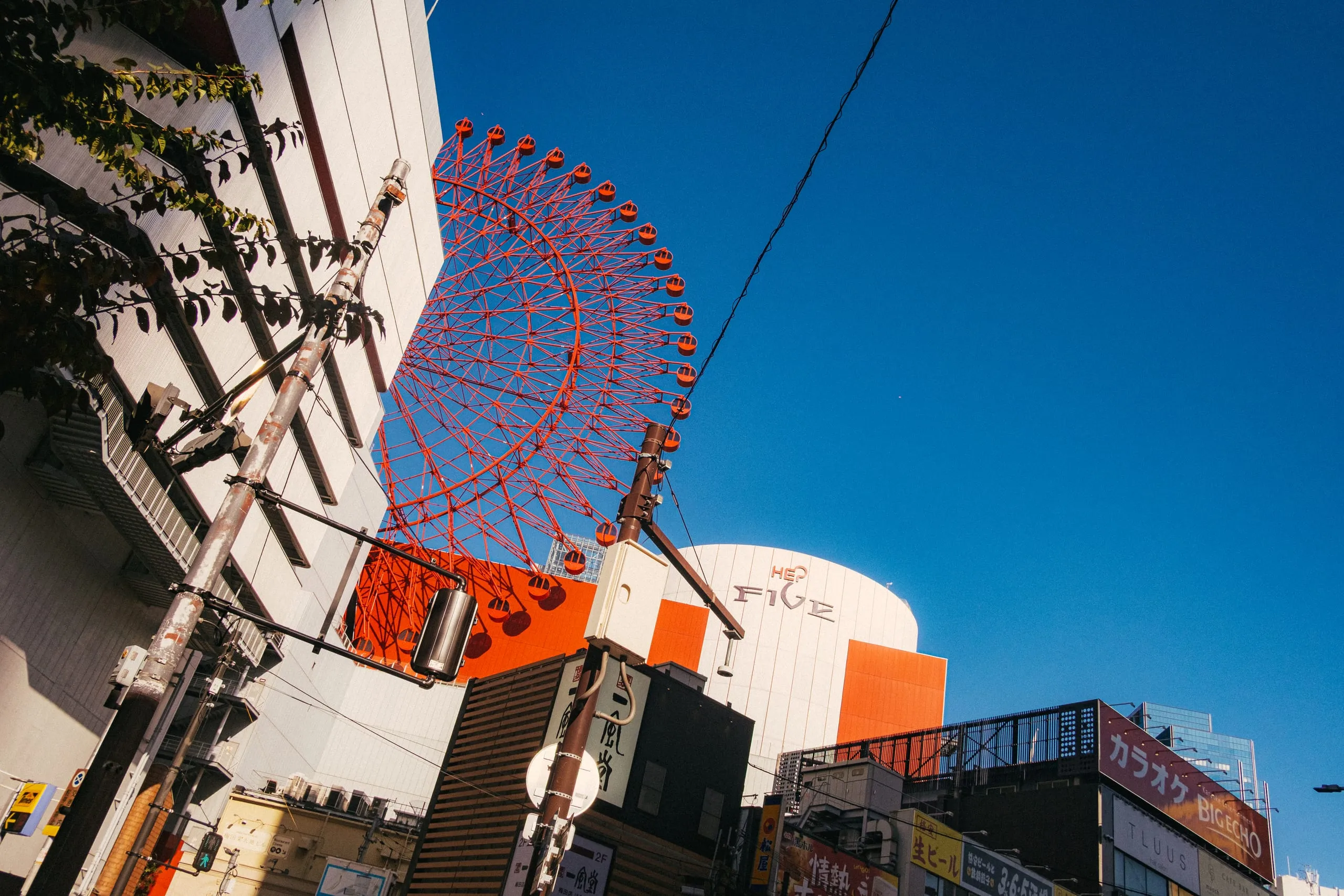 A red Ferris wheel rising above shopfronts against a blue sky