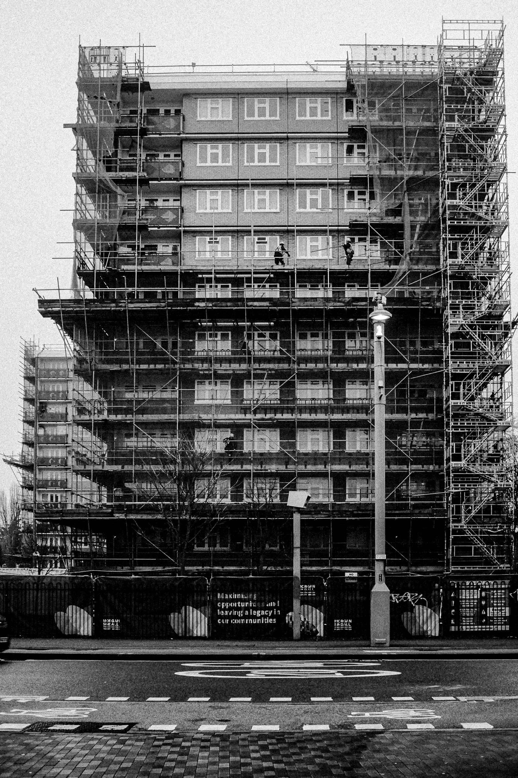 Two men install scaffolding on a social housing estate, Lea Bridge Road