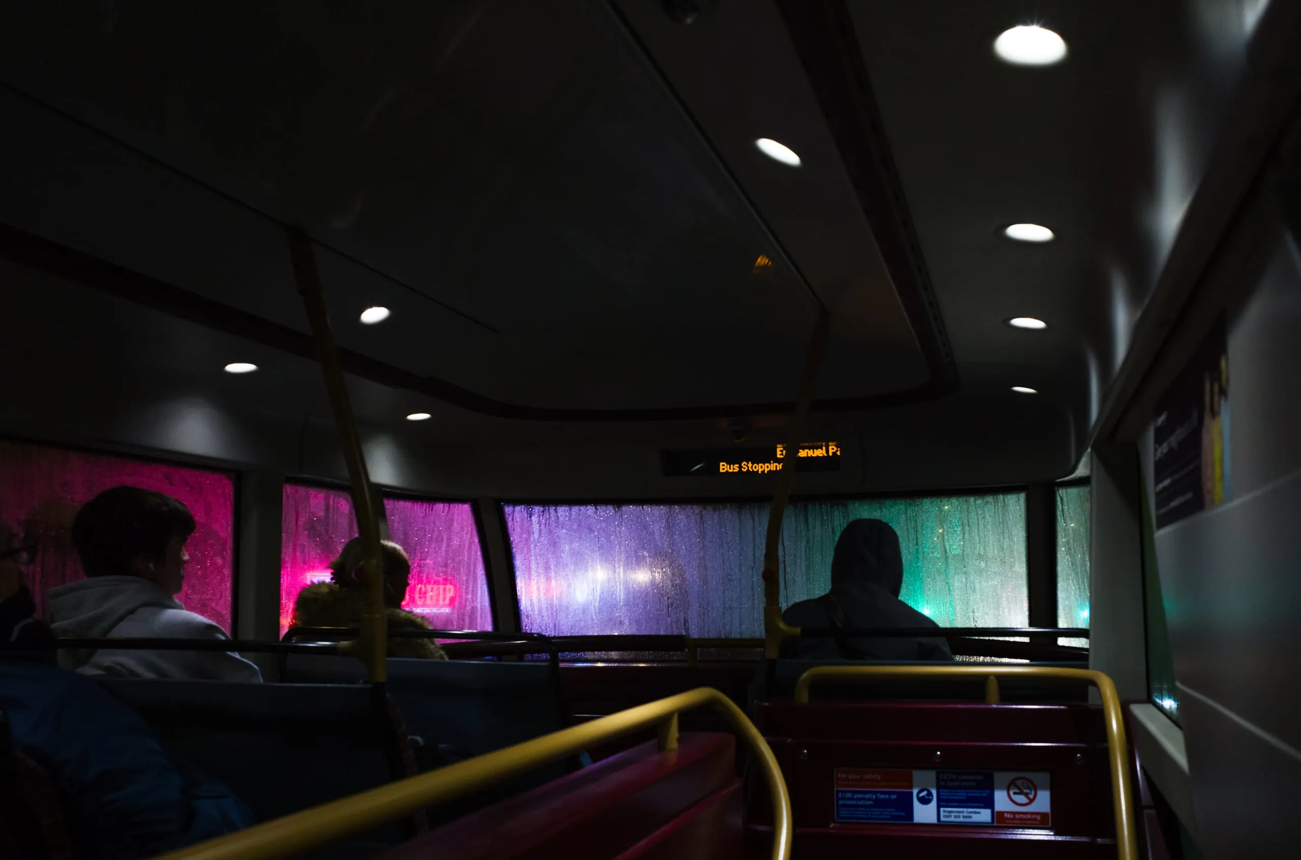 Passengers on a bus at night, rain on the windows lit by streetlights