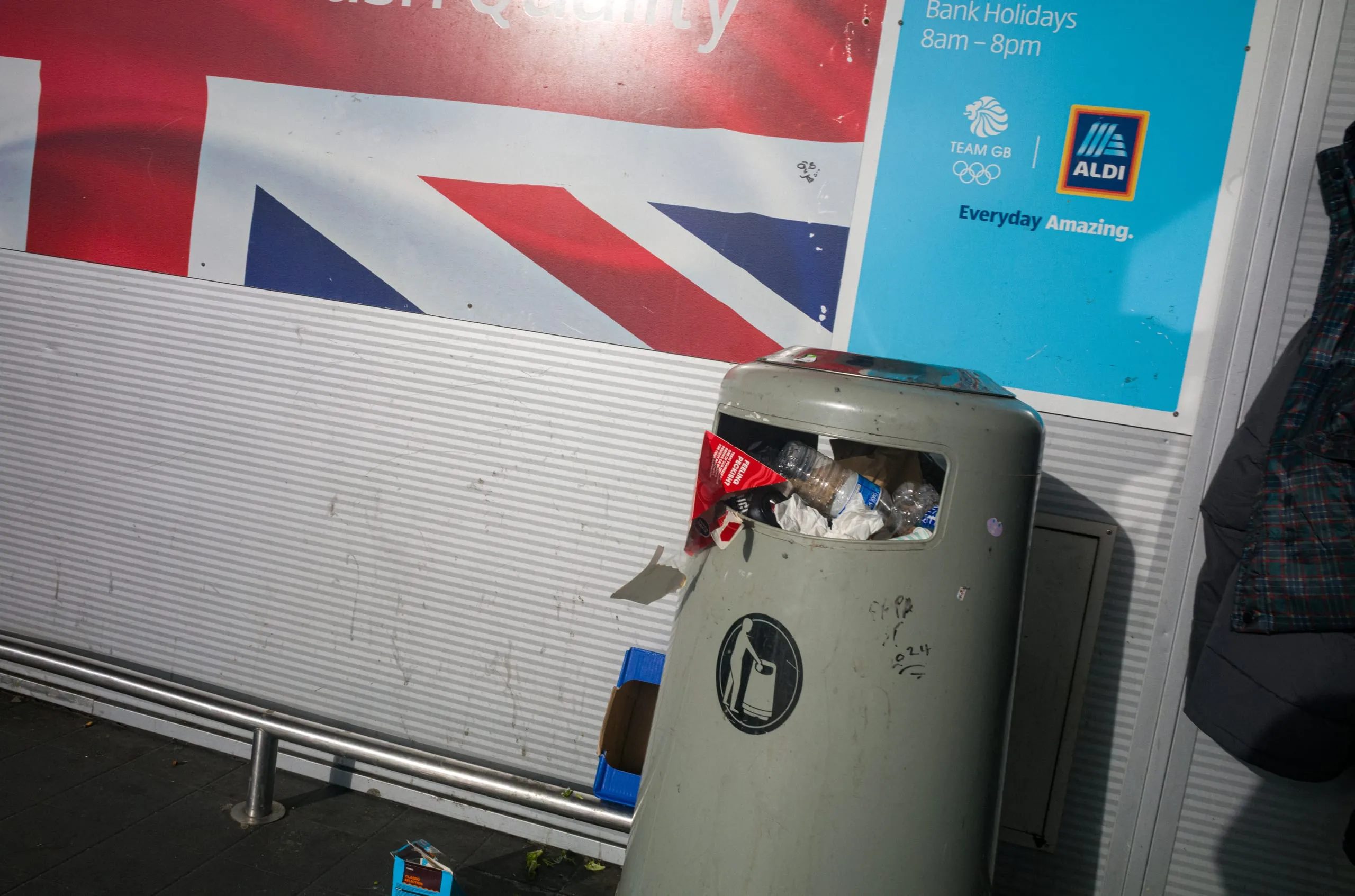 An overflowing litter bin against an Aldi advertising hoarding