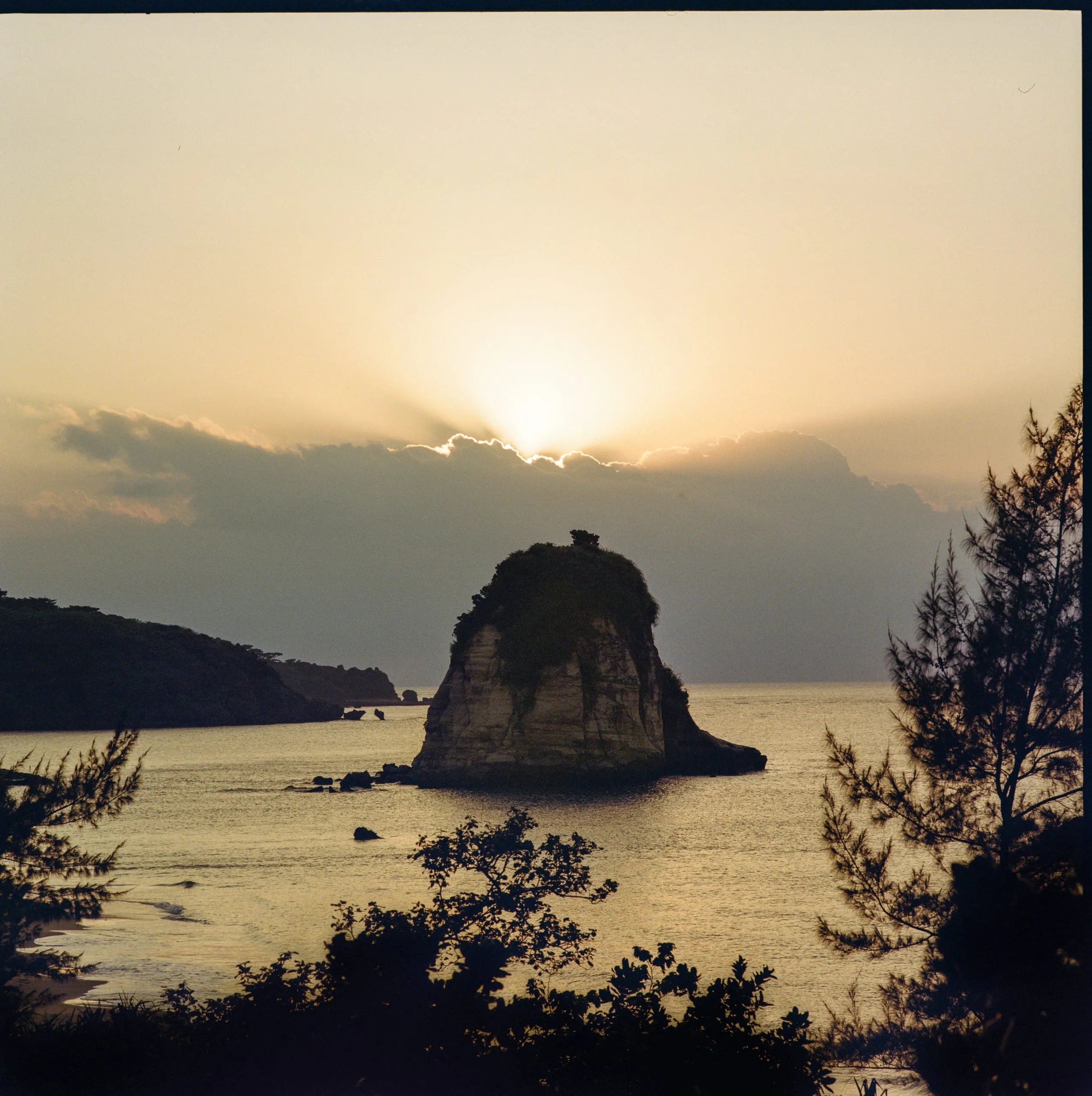 A view of the sun setting behind a sea stack in Tsukigahama beach