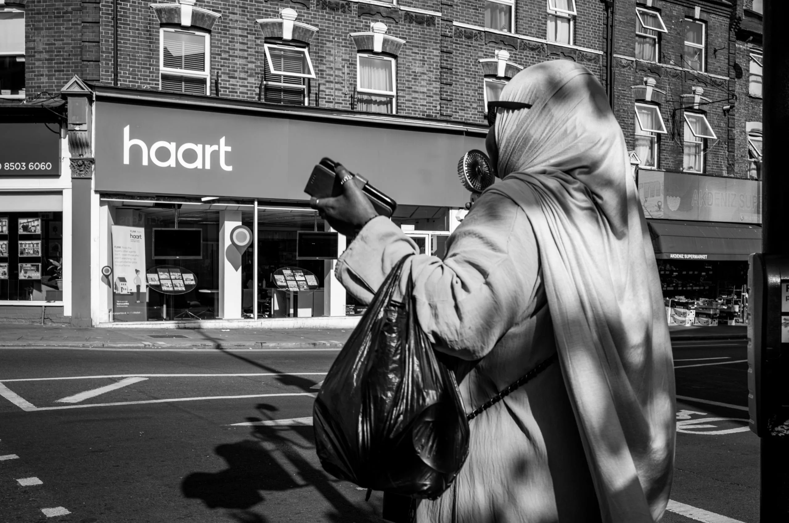 Woman using electric hand fan while crossing the street on the phone, Walthamstow