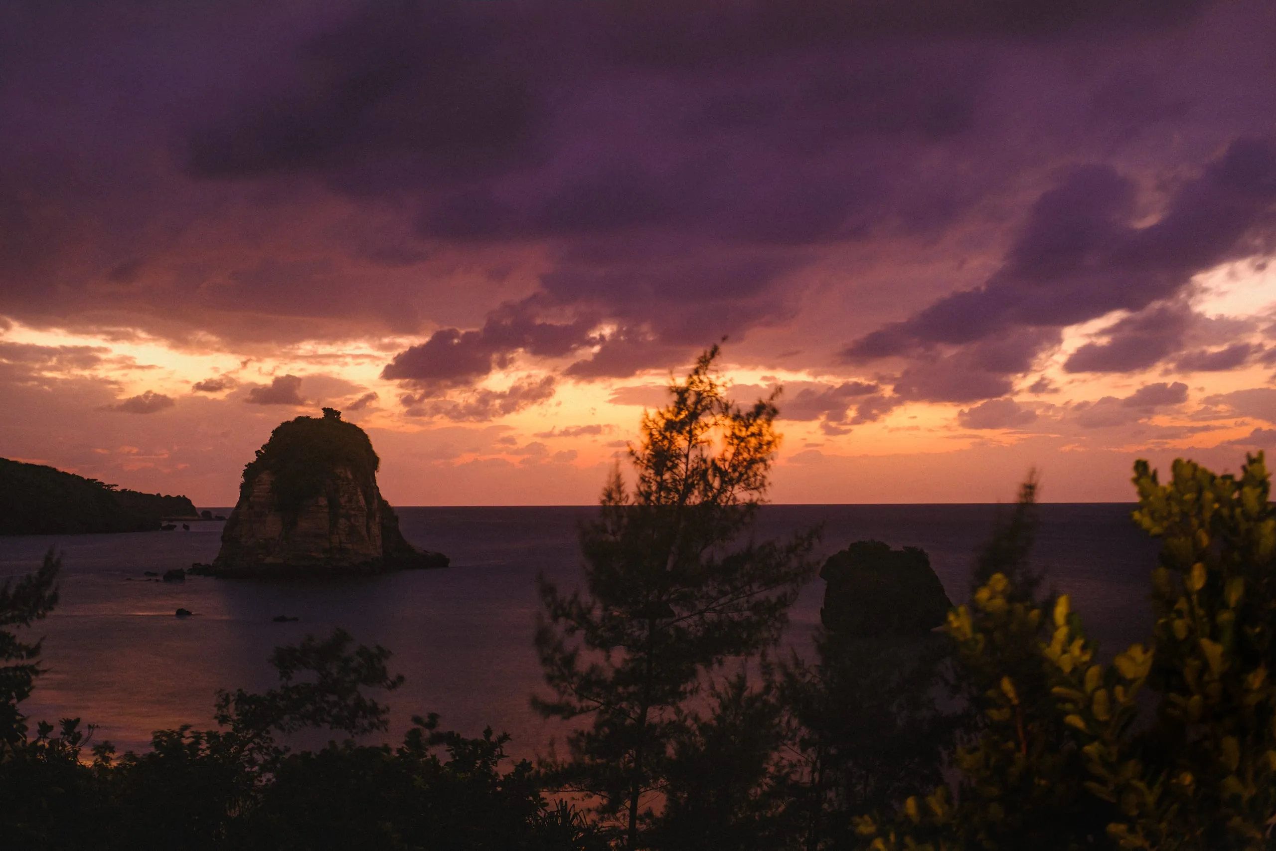 An offshore rock and sea cliffs at dusk under a coloured sky, Japan