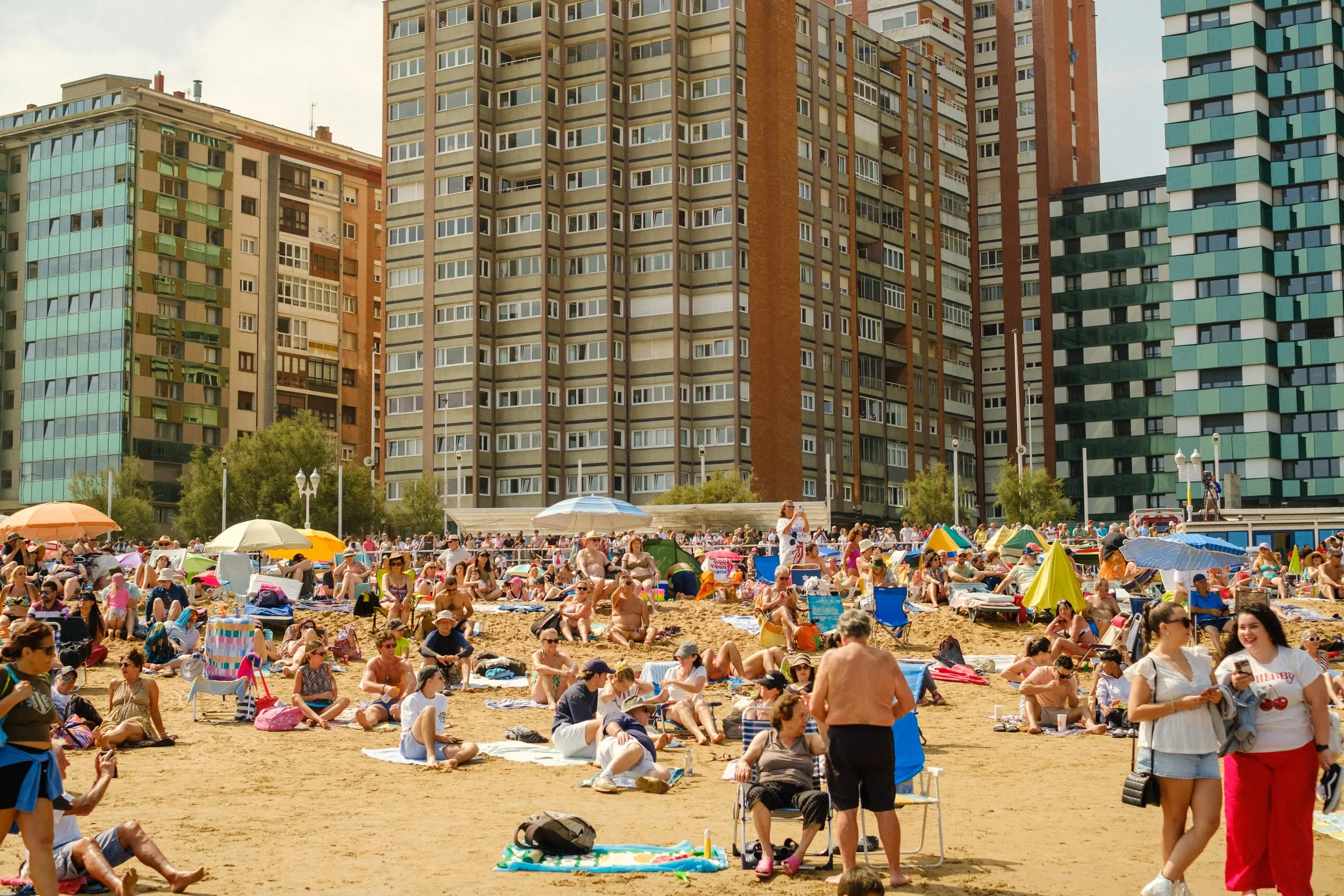 Sunbathers fill a beach beneath high-rise apartment blocks