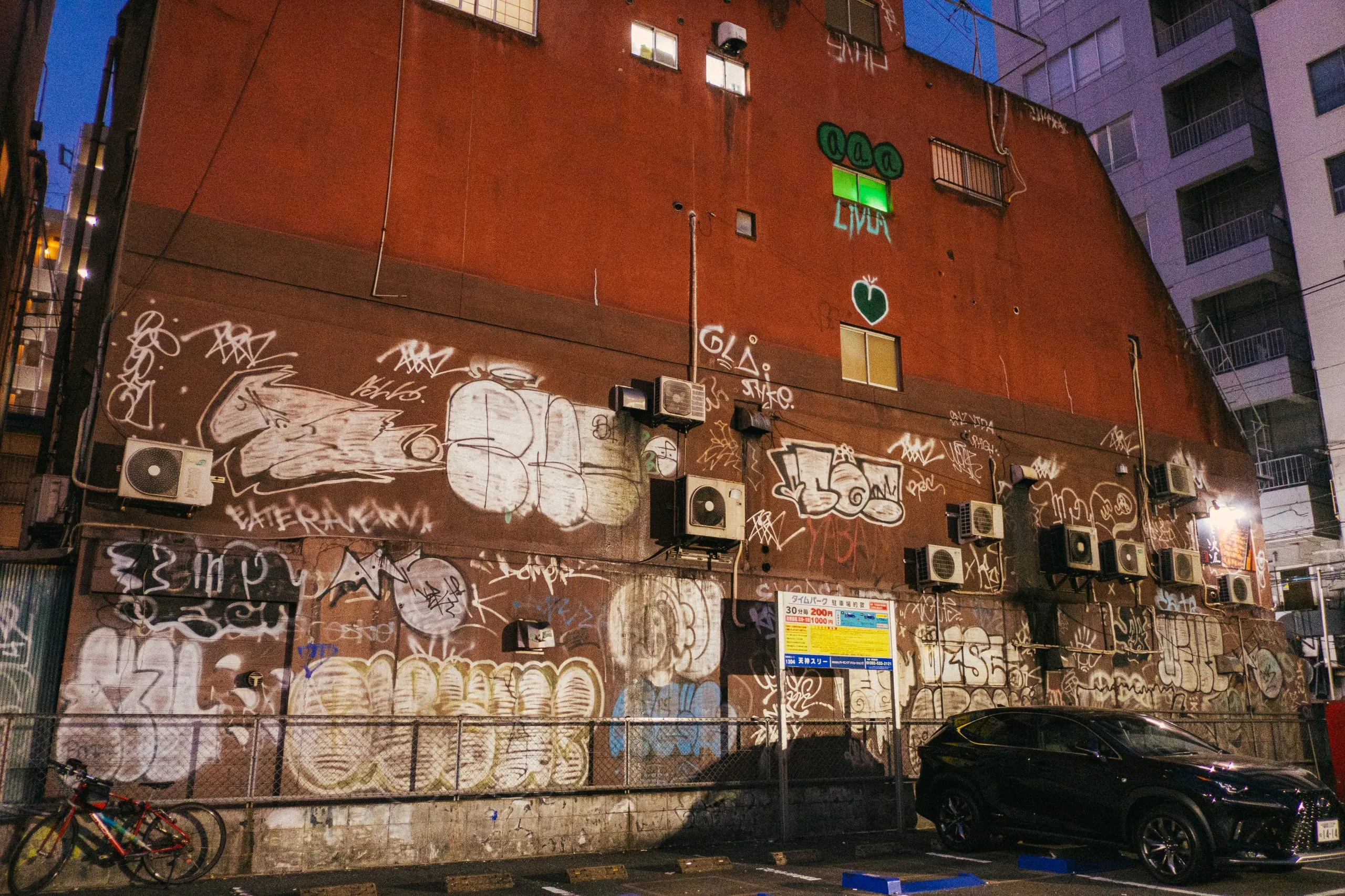 A graffiti-covered building wall above a parking lot at night