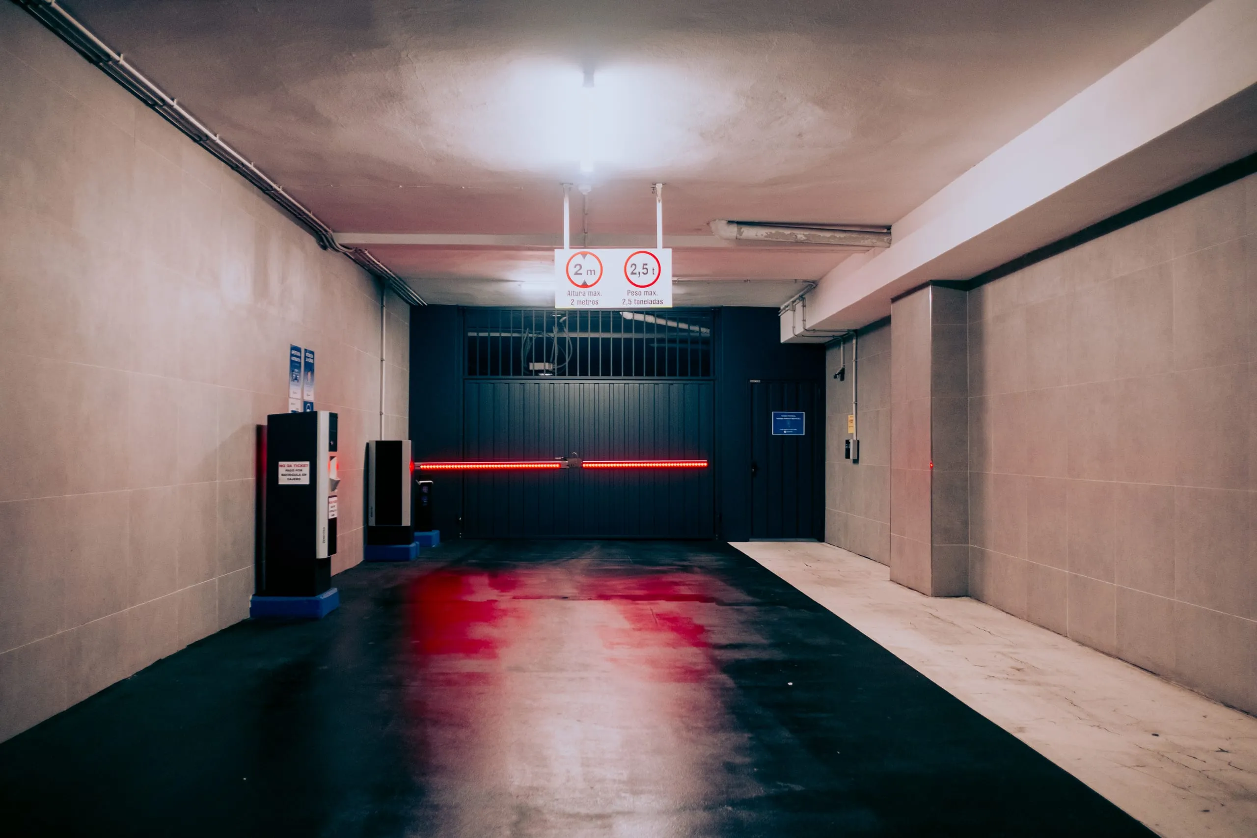 A height-restriction sign and red barrier light at the entrance to an underground car park