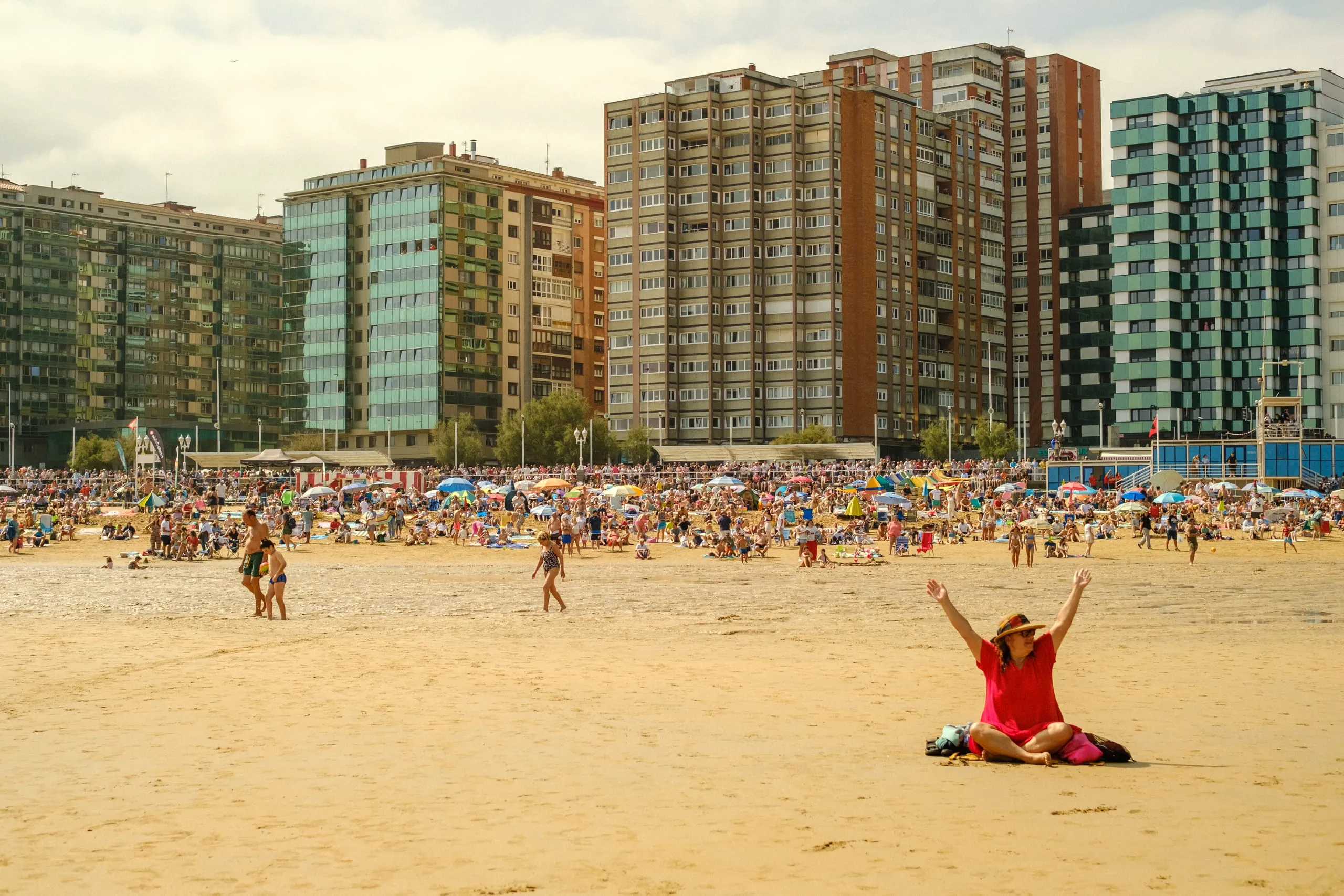 A woman in red sits on a beach waiting for the beginning of the Gijón Air Show