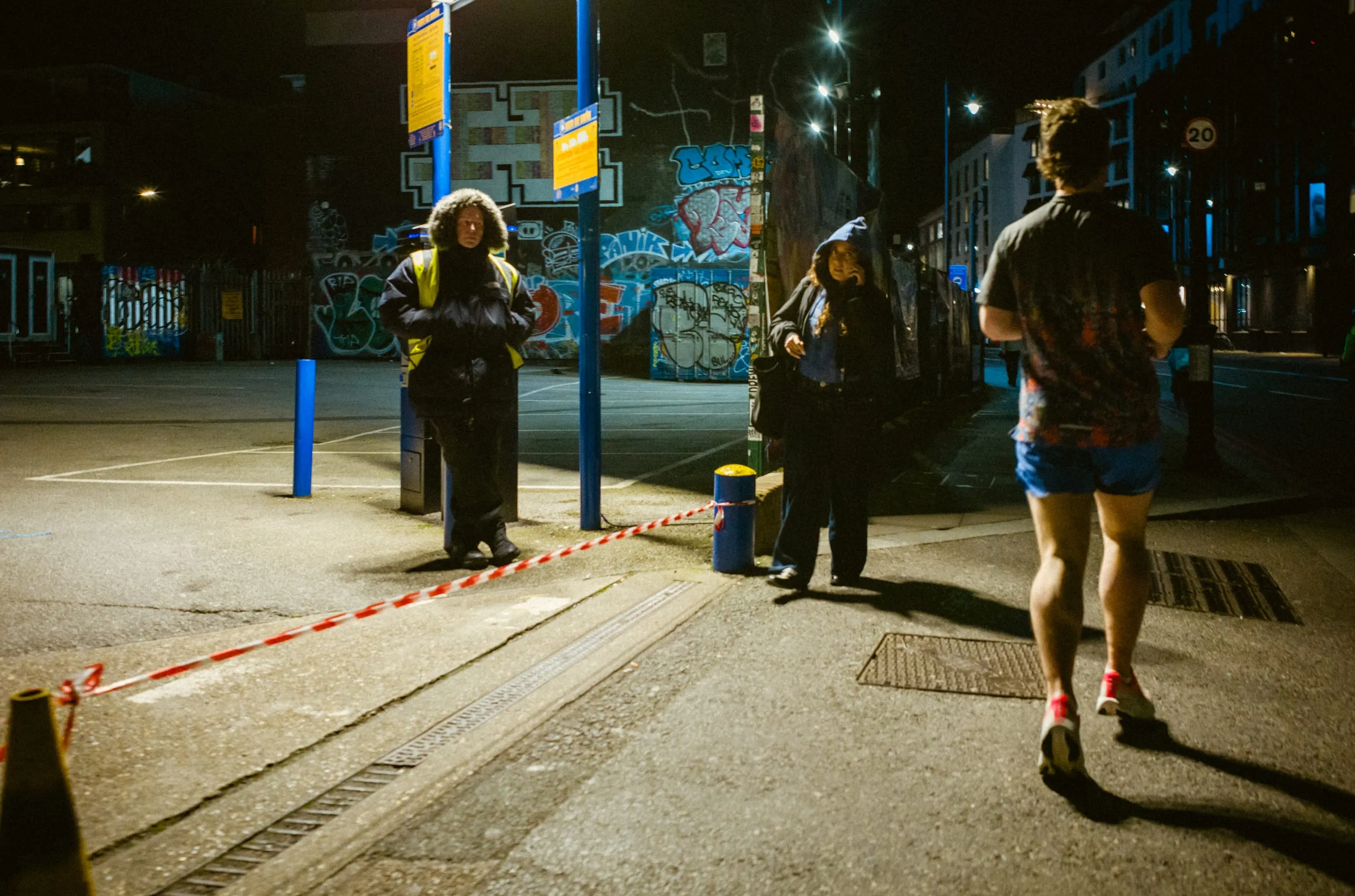 People wait at a bus stop at night as a man runs past, London