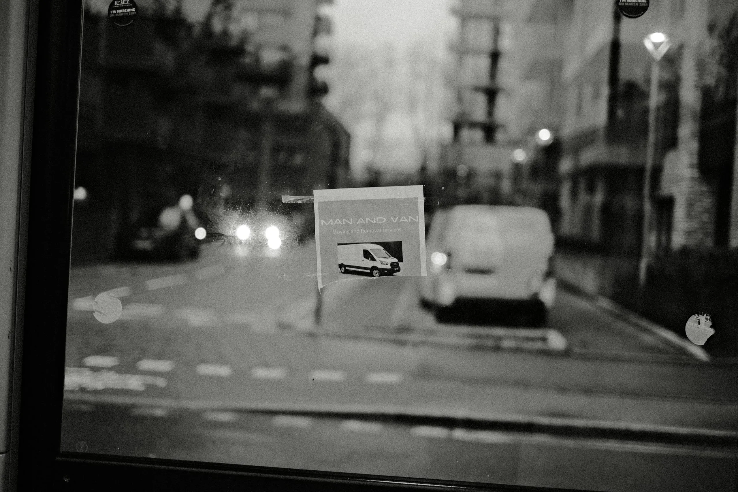 A van and street reflected in a bus shelter window carrying a 'Man and Van' advert