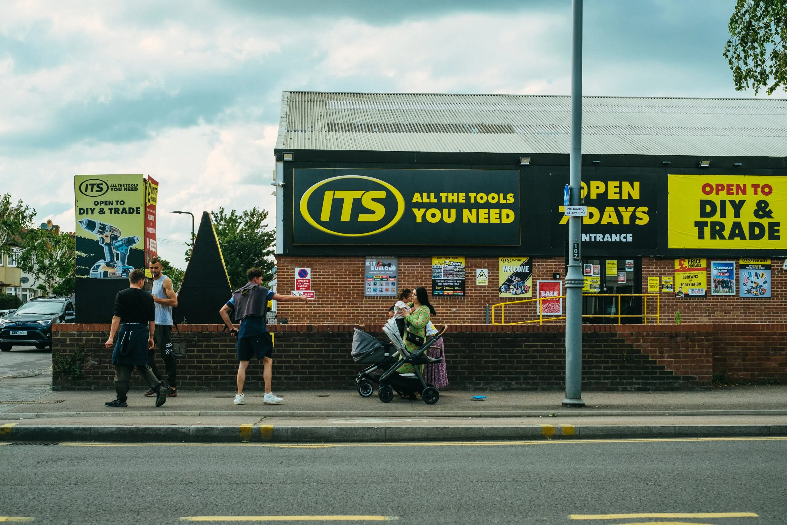 A man and a mother interact in front of a hardware shop, Lea Bridge Road