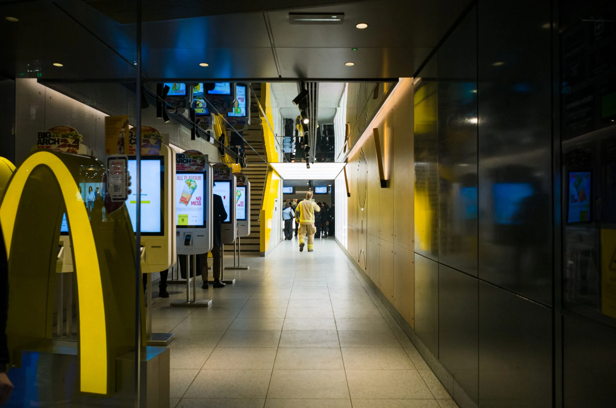 A fireman walks down a corridor past McDonald's self-order kiosks