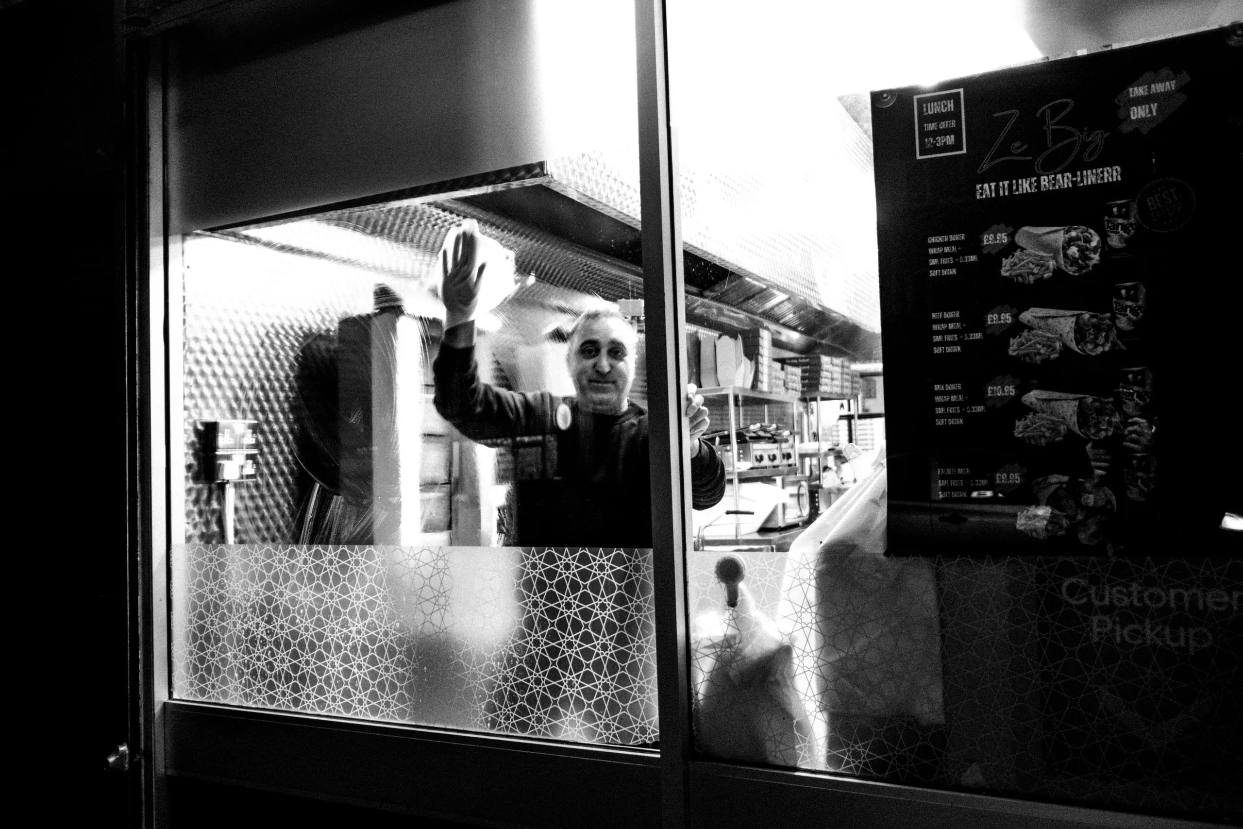 A man cleans the inside of a takeaway kebab shop window front at night