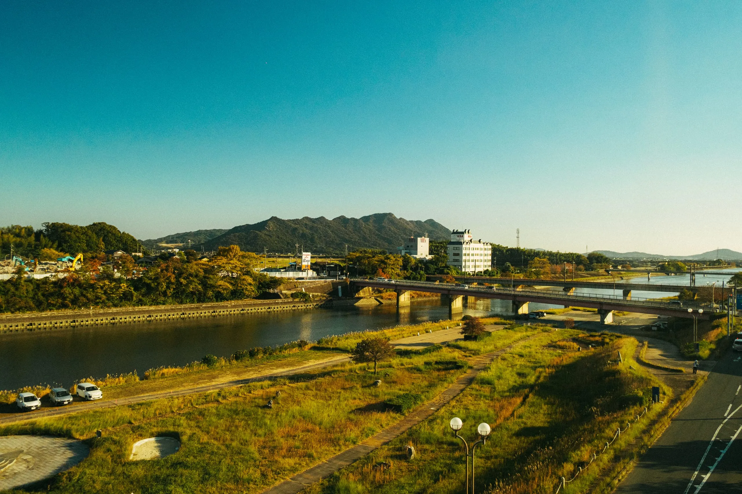 A bridge over a river with hills behind a small town as seen from the Shinkansen