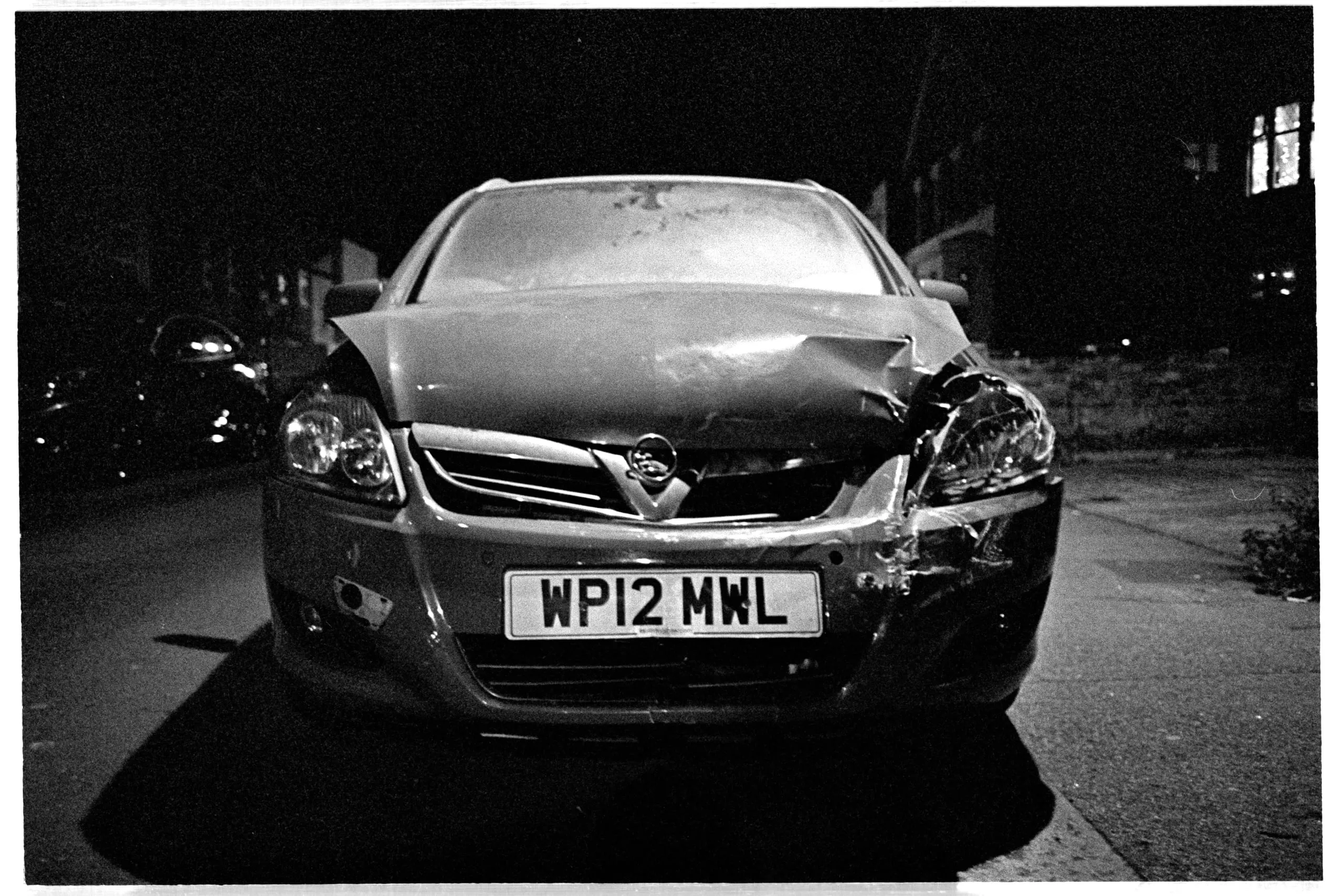A parked car with a crushed front wing and bonnet at night