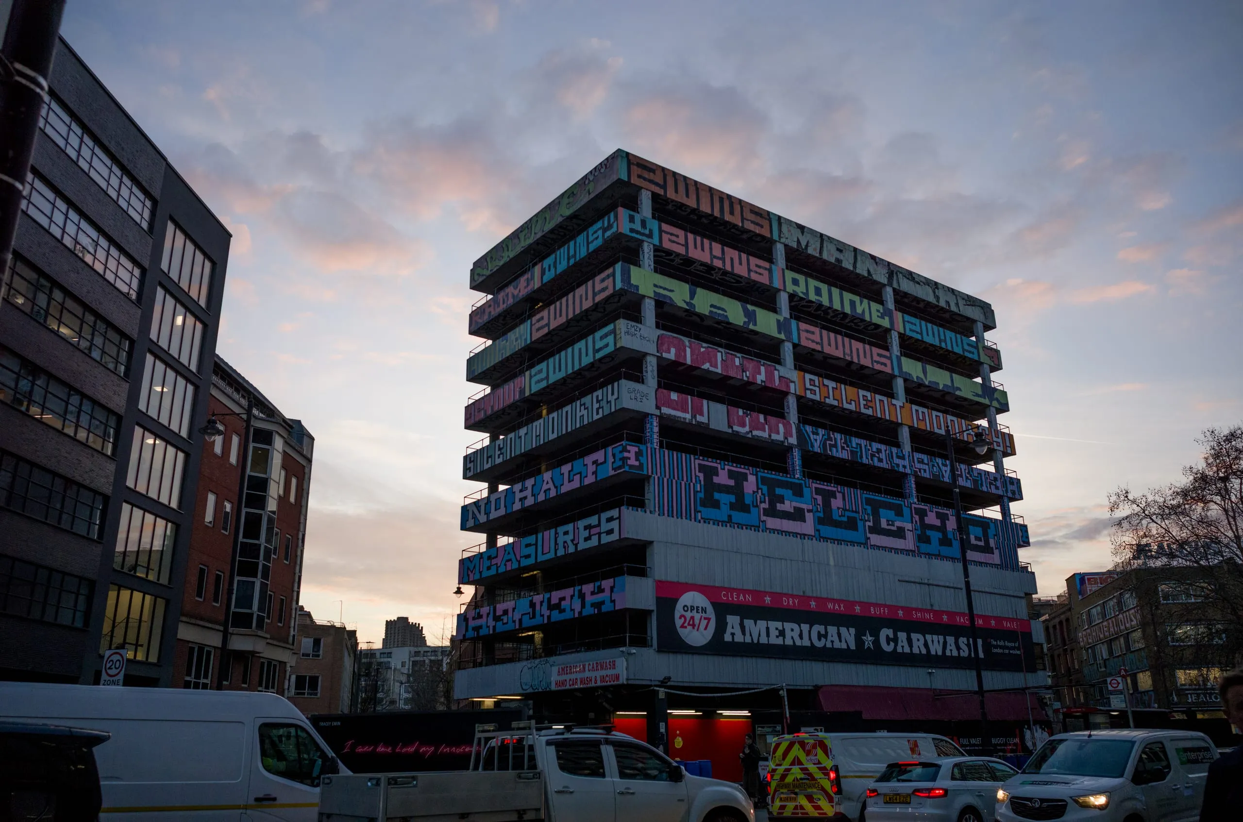 A building covered in painted lettering above an American Car Wash at dusk, with traffic below, London