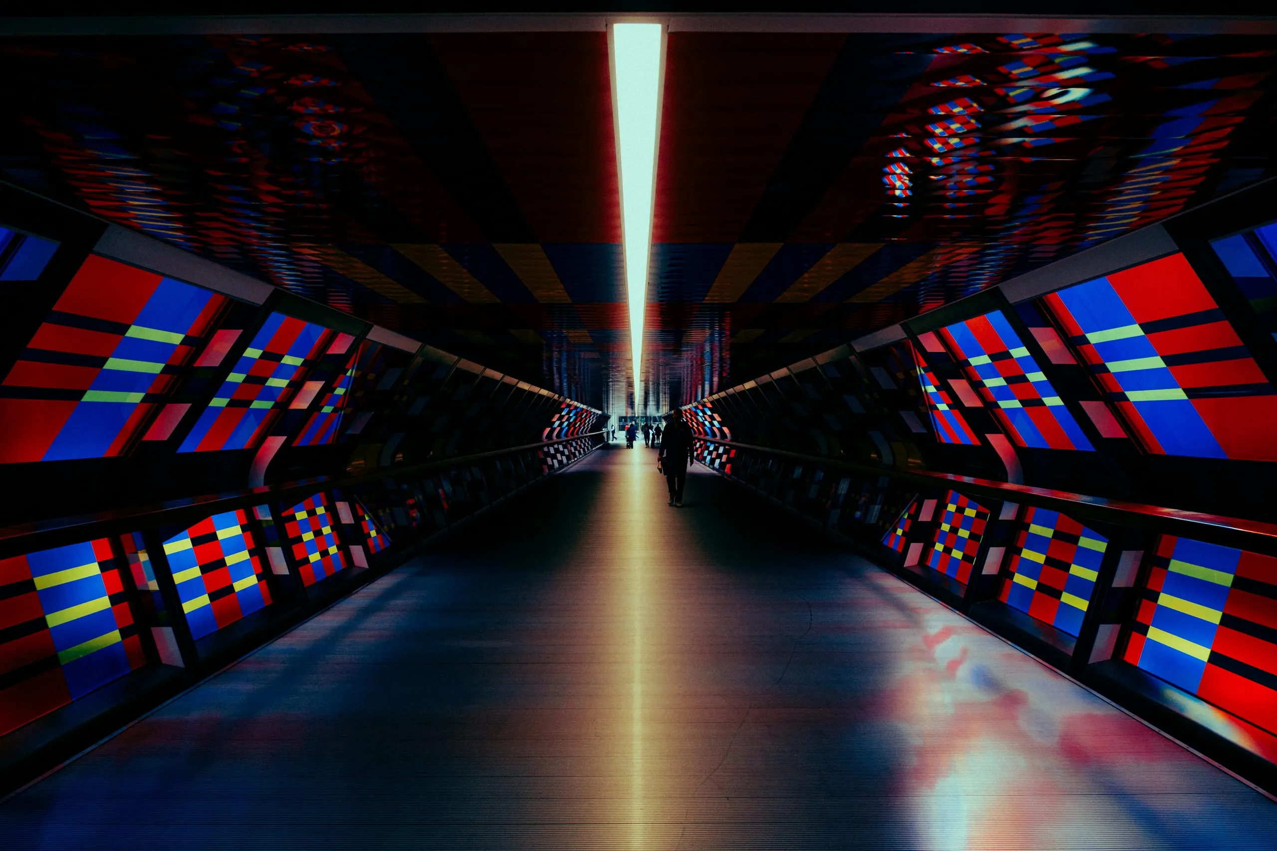 A lone figure walks through the tiled, brightly coloured Adams Plaza Bridge tunnel, Canary Wharf