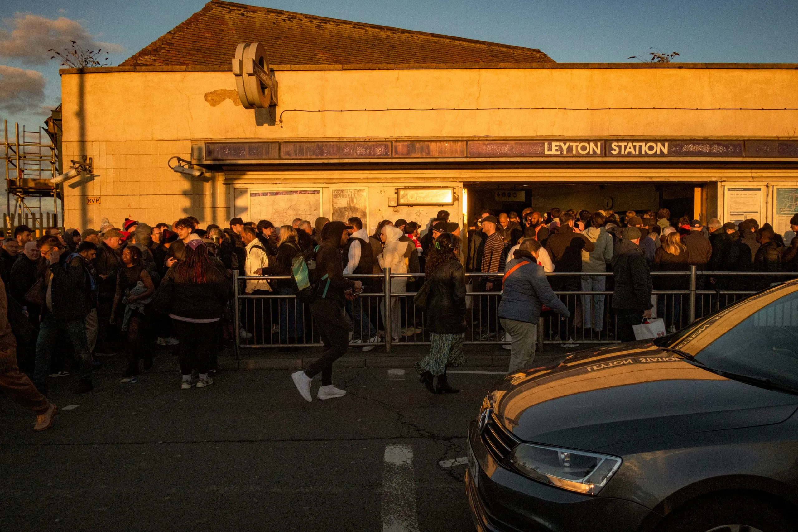 A football crowd gathers outside Leyton station in the evening light, Leyton