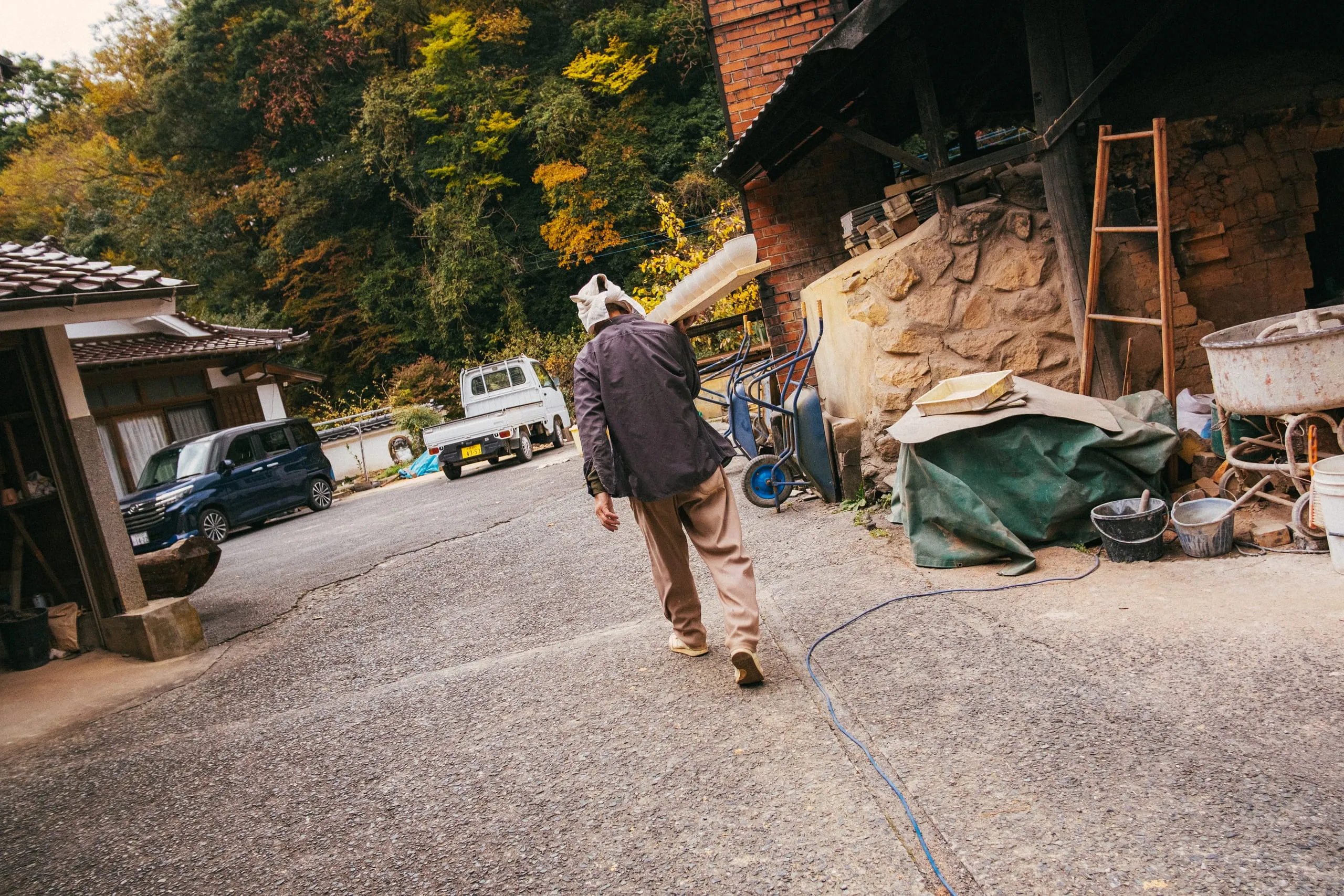 An man carries a row of ceramic bowls to a kiln