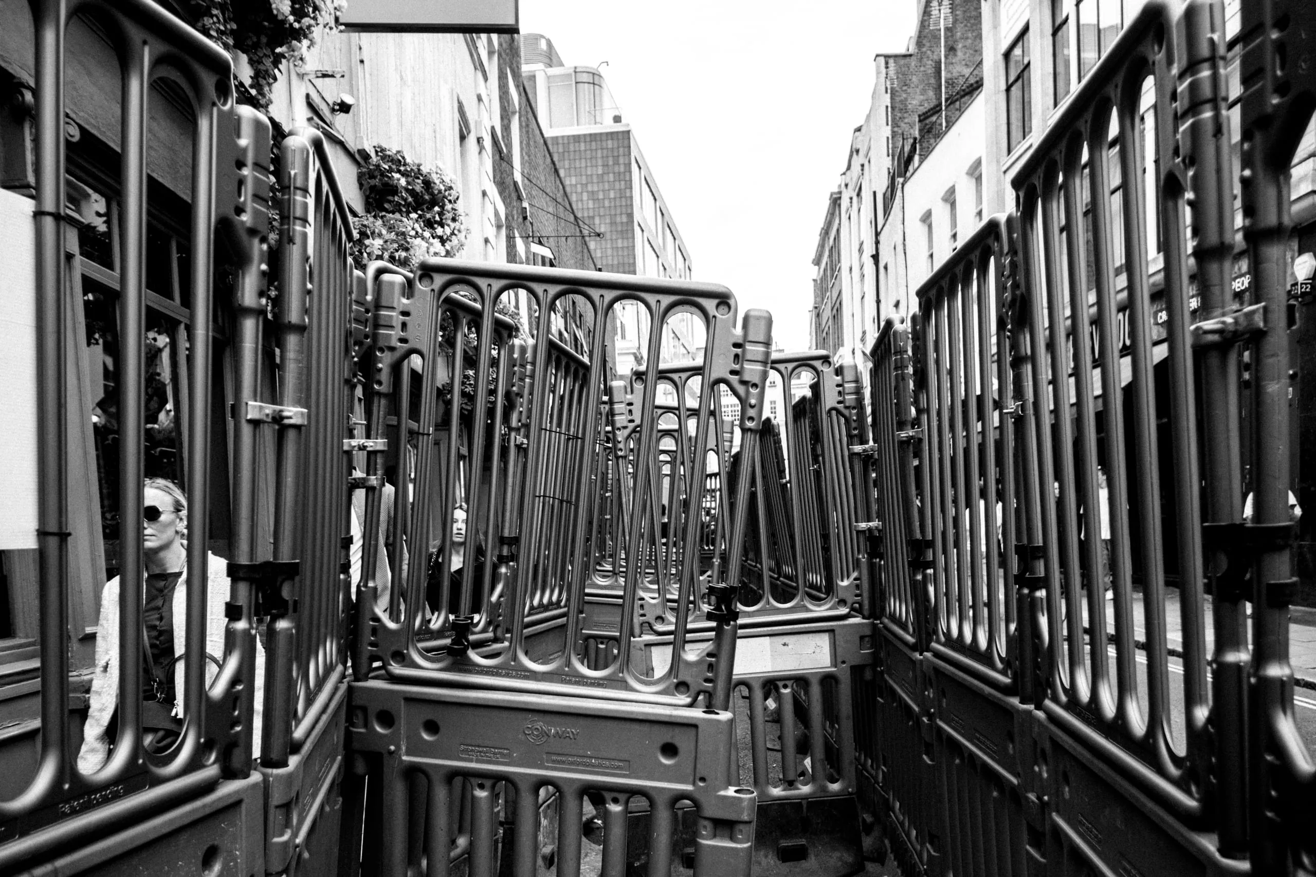 A woman stands among stacked plastic crowd barriers, Soho