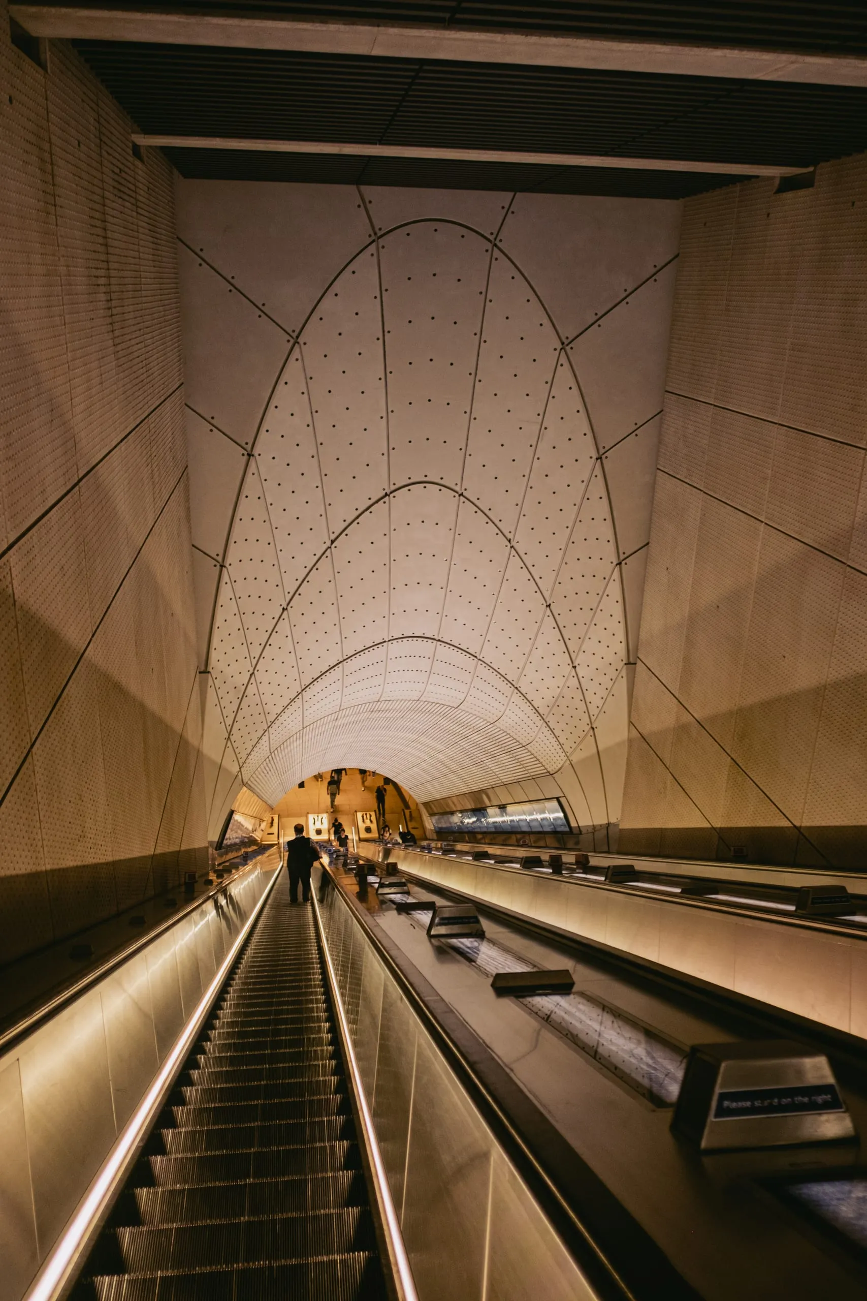 A passenger rides the escalator under the vaulted ceiling of the Whitechapel Elisabeth Line Station
