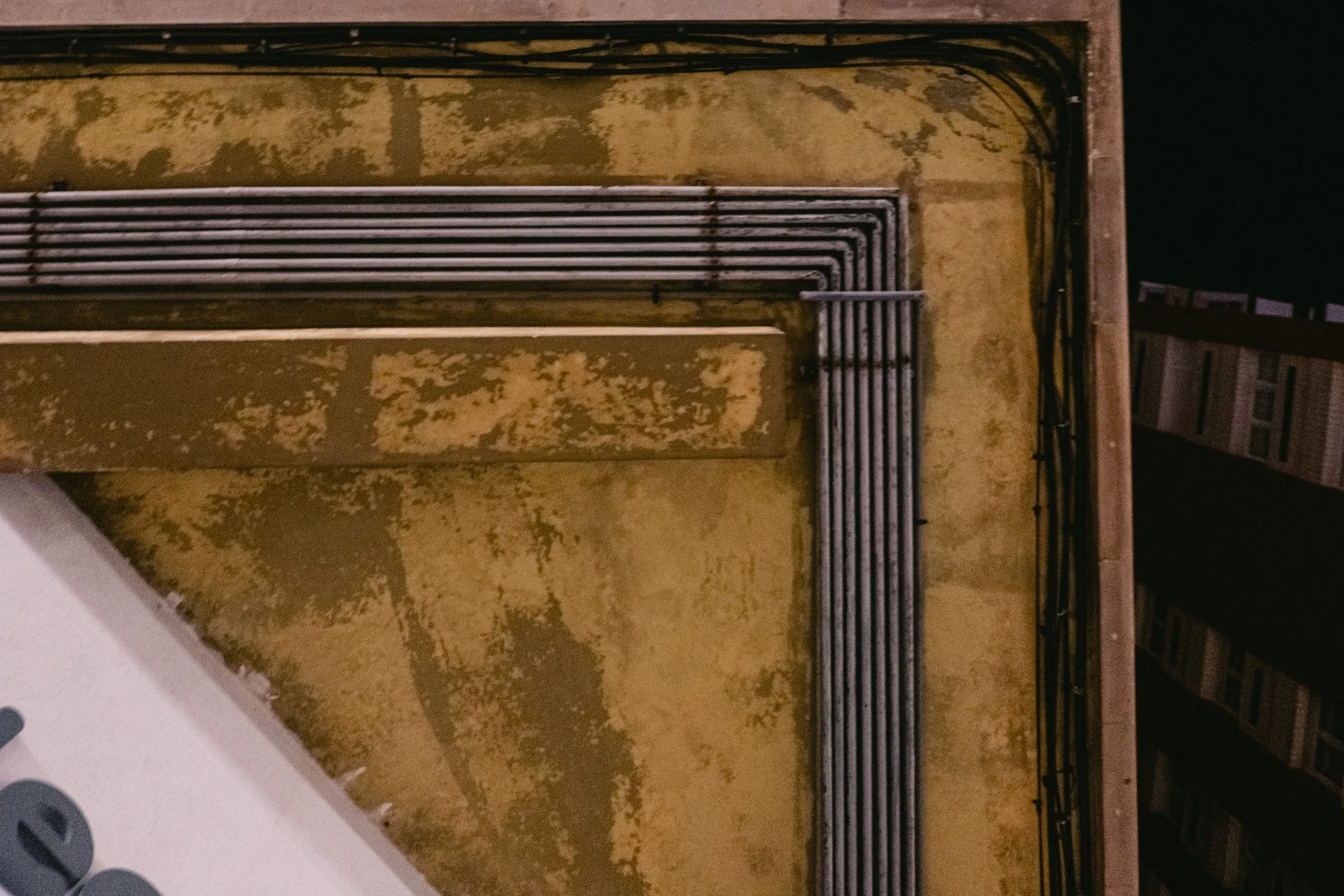 Conduit pipes bend around the corner of a stained wall on a rooftop