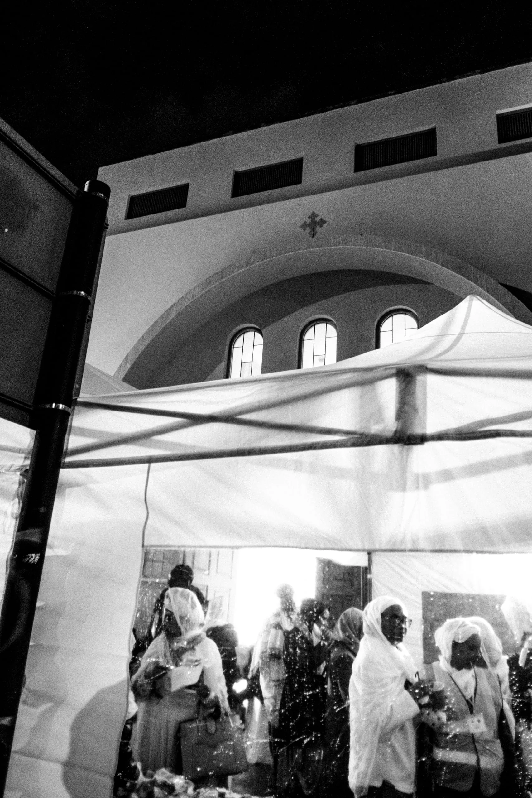 Worshippers in white headscarves gather under a marquee outside a church at night