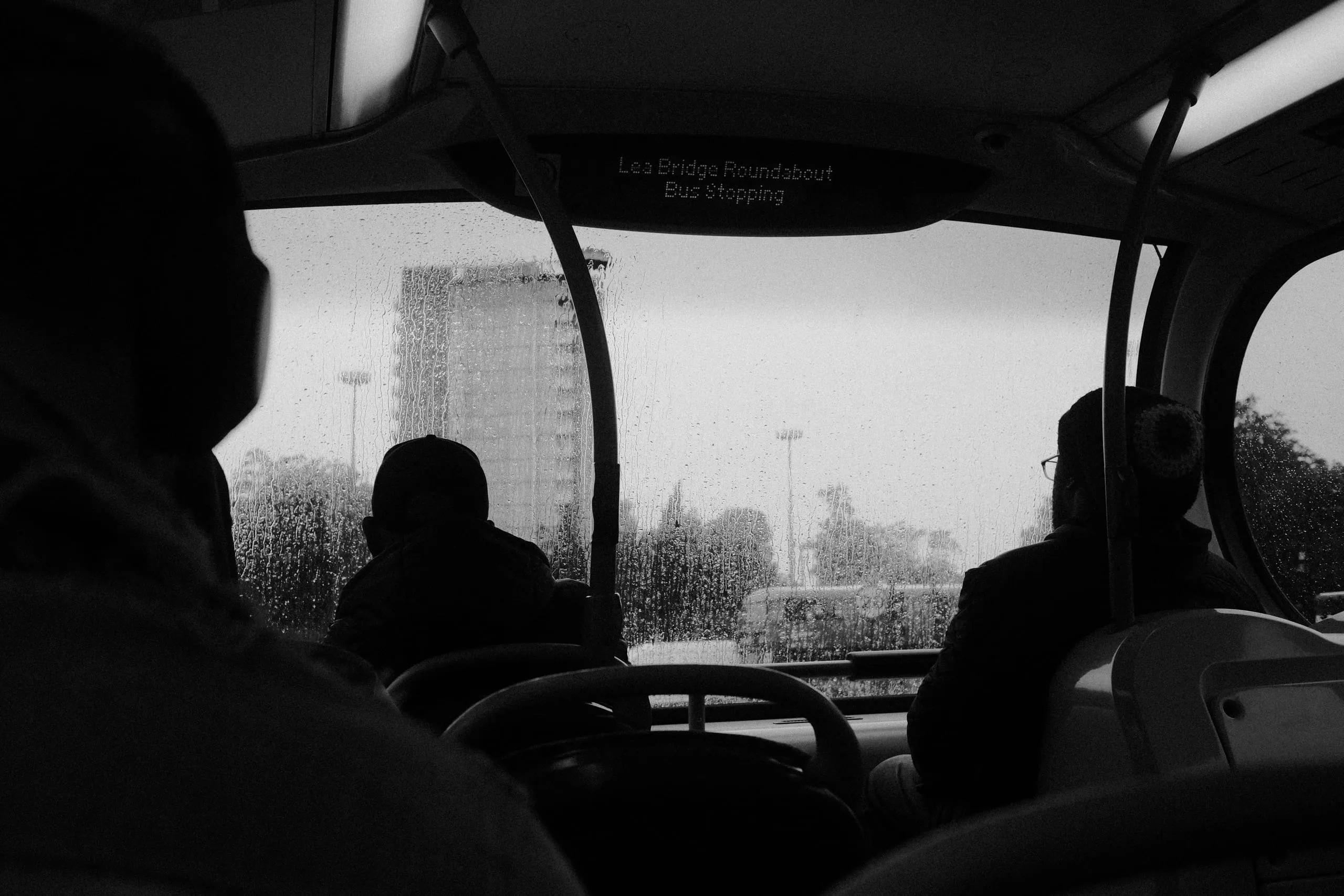 Passengers ride a bus past a tower block in the rain, the display reading Lea Bridge Roundabout