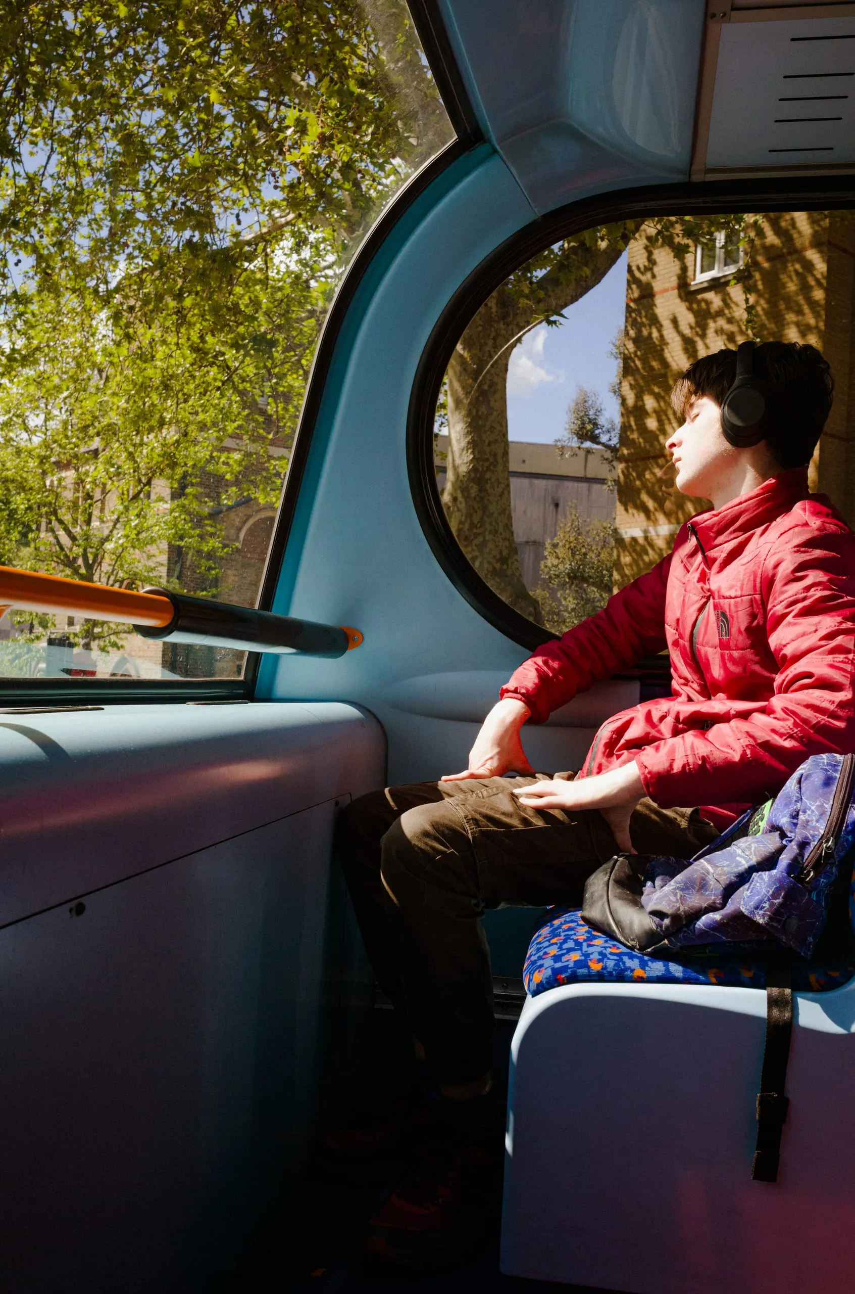 A young man in a red jacket listens to music in spring sunlight