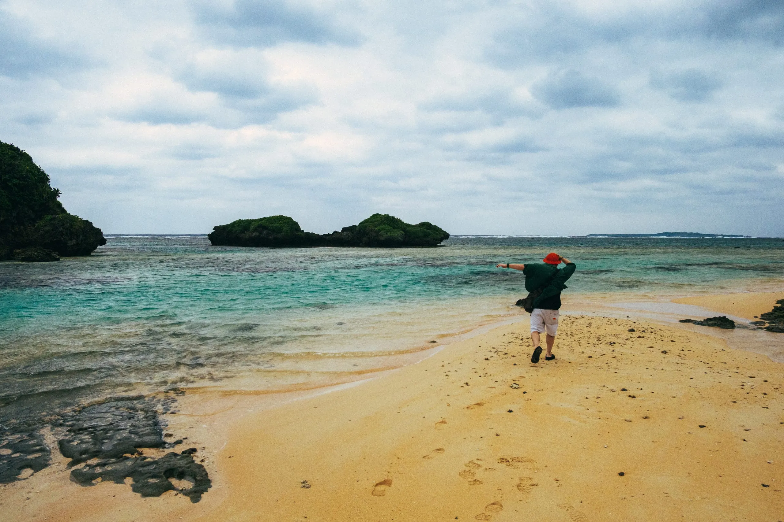 A person walks along a sandspit between rock outcrops on a beach, Japan