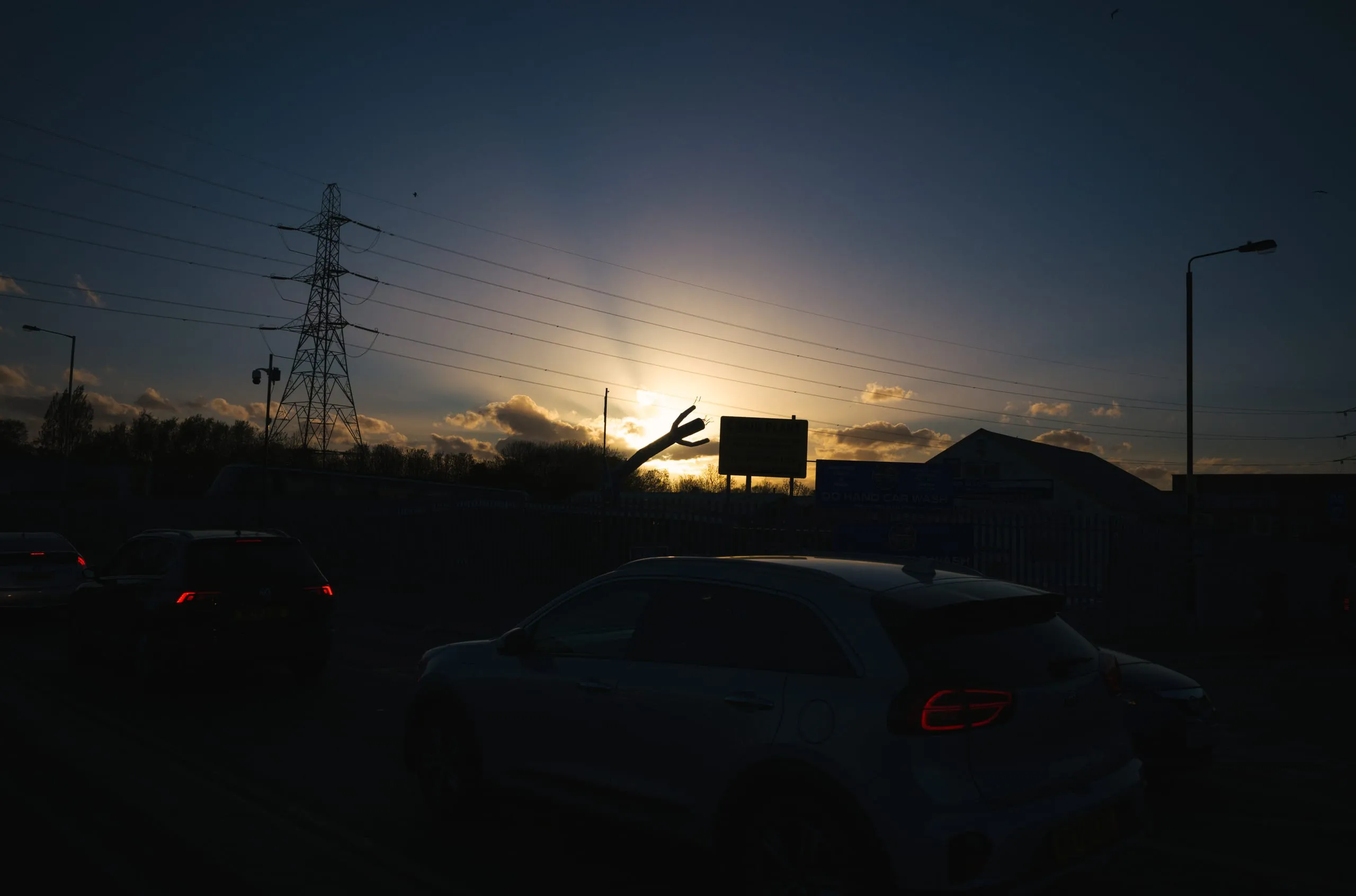 Silhouetted cars and a pylon at a hand car wash at dusk