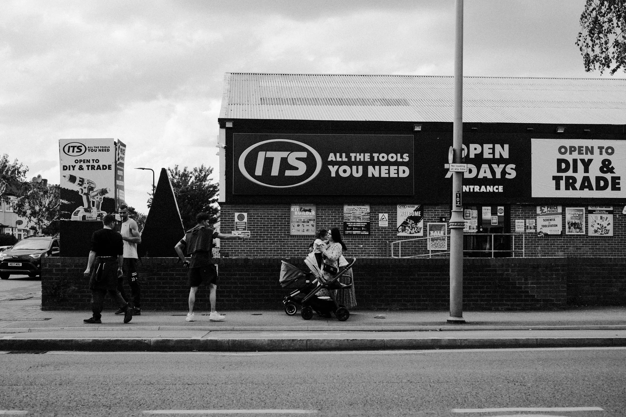 A man gesticulates at a woman in front of a DIY Shop, Lea Bridge road