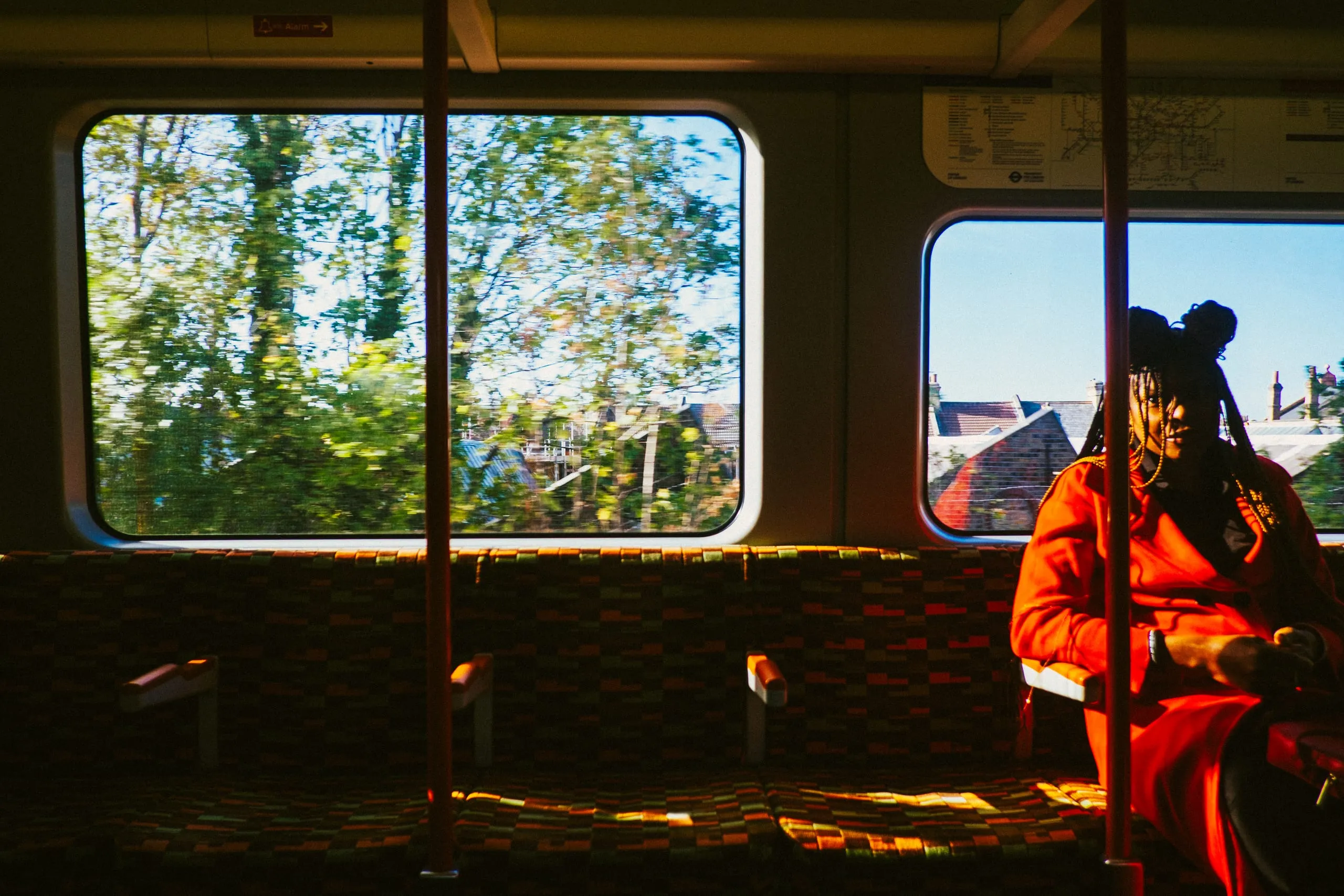 A woman in an orange coat sits by the window of an overground train