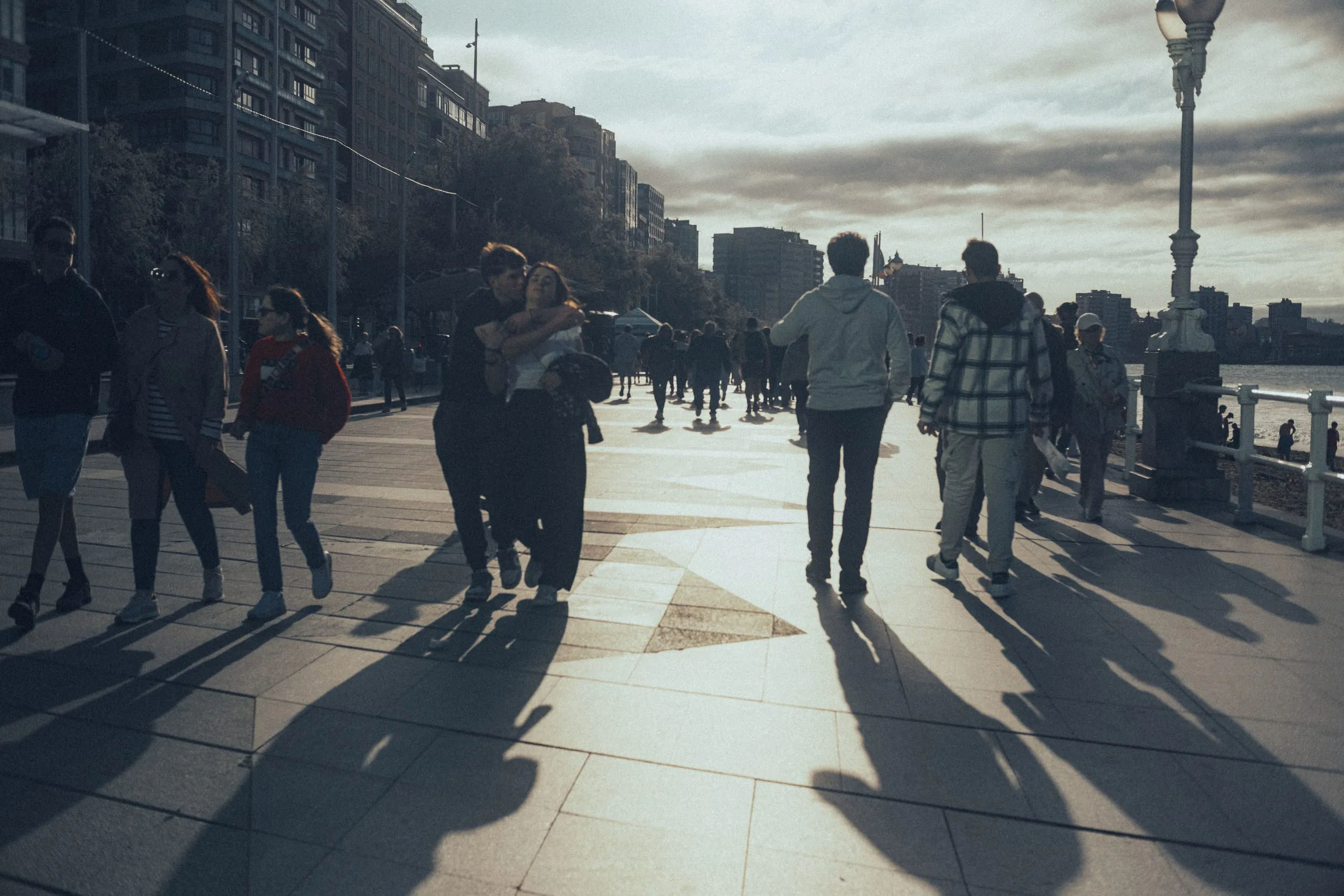 A heterosexual couple embrace as they stroll along the Gijón promenade