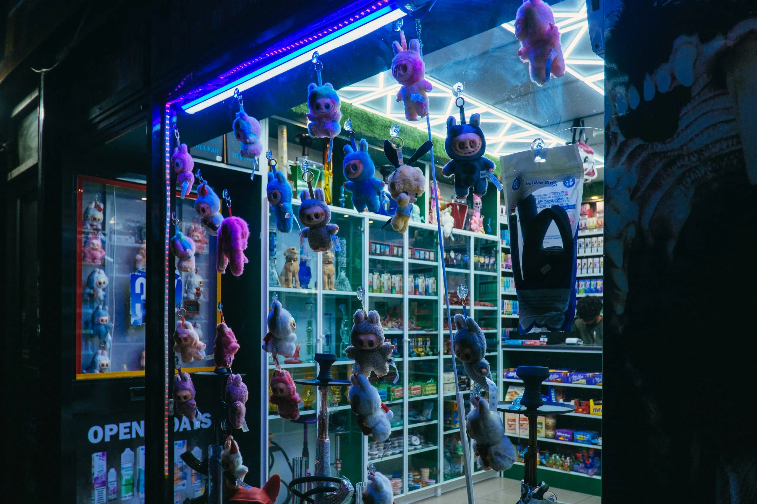 Labubus hang in the lit window of a shop at night