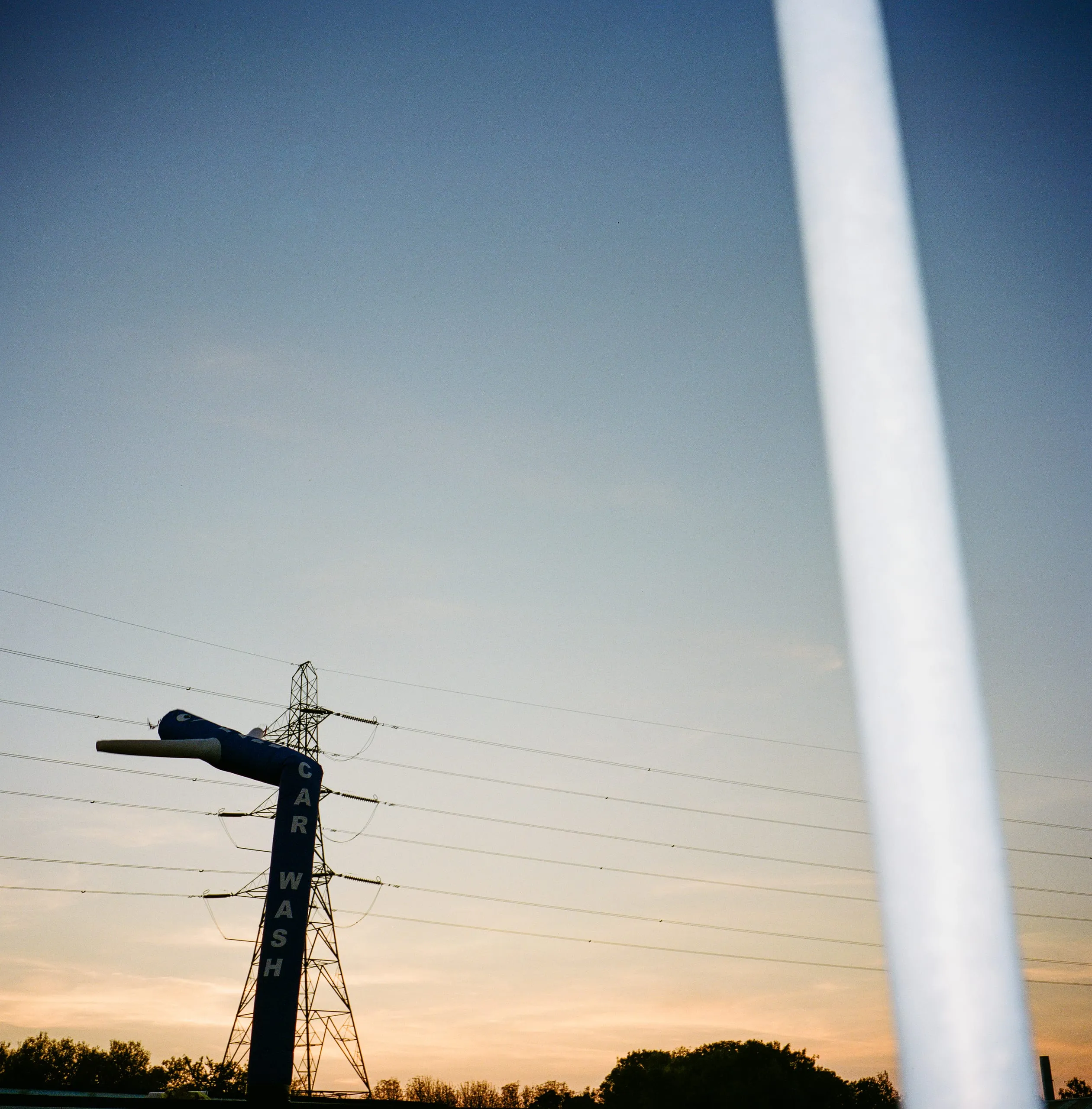 A 'Car Wash' inflatable tube man and an electricity pylon silhouetted against the dusk sky