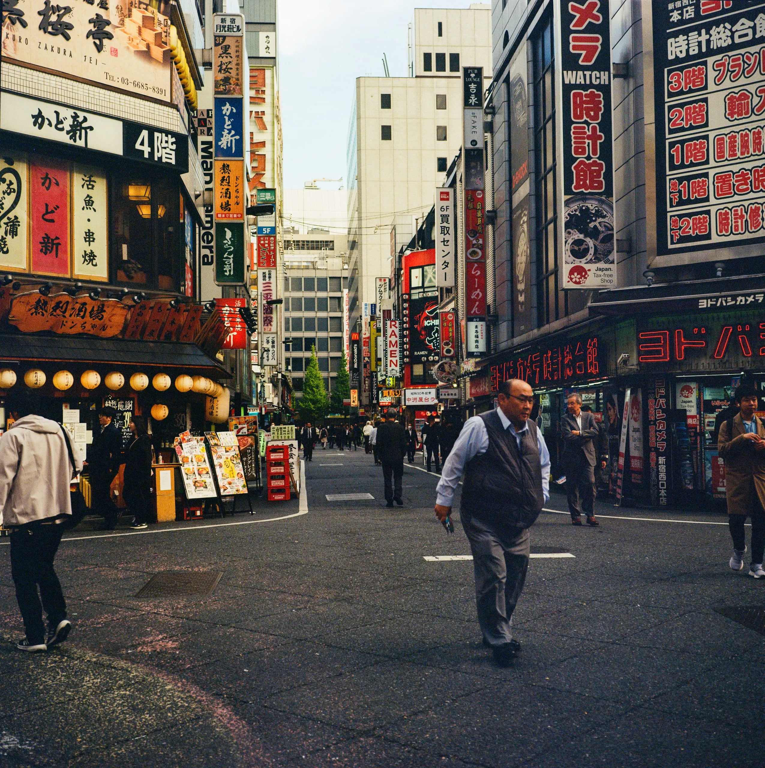 A man crosses a street lined with neon signs in Shinjuku camera quarter