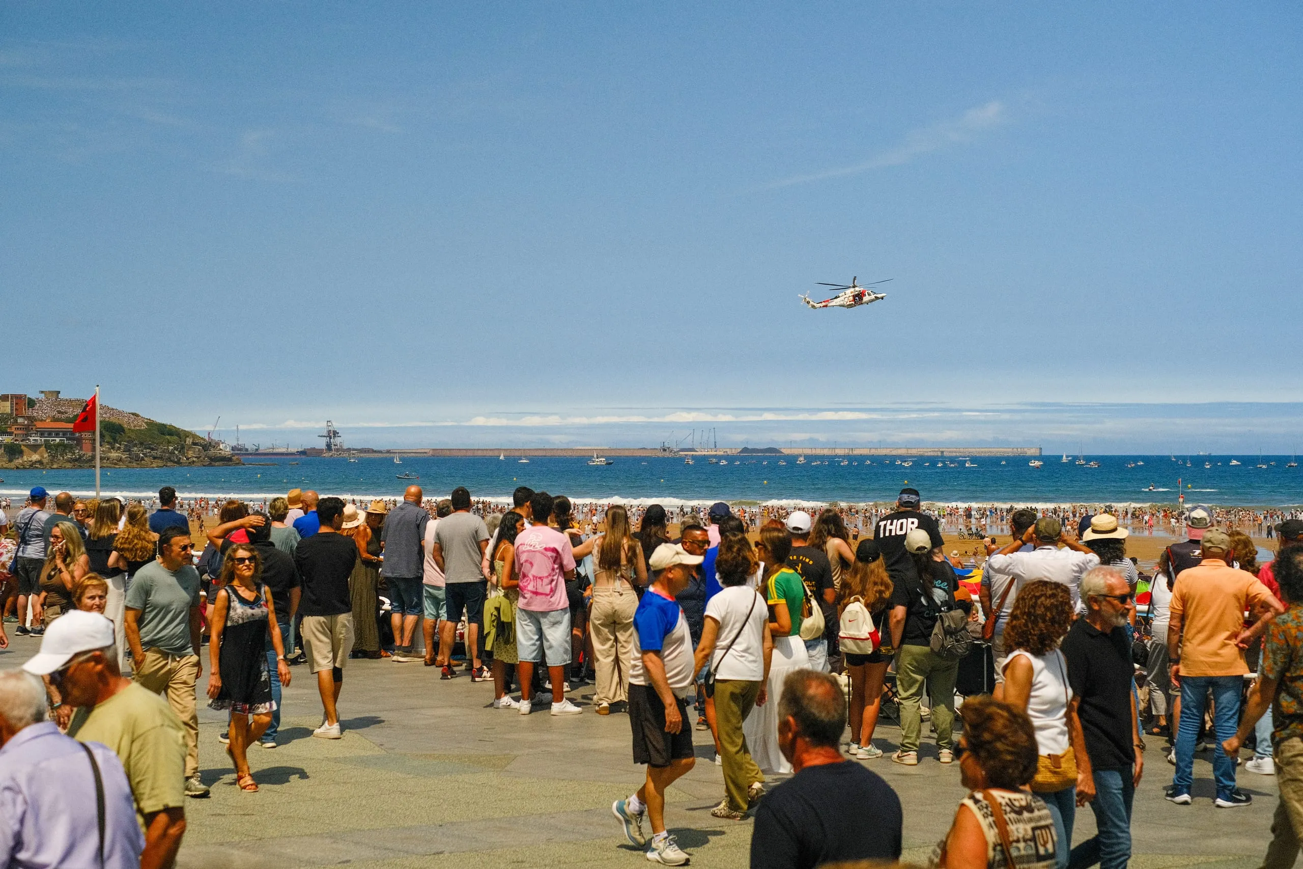 A crowd on the seafront watches a helicopter fly over the bay at the Gijón Air Show