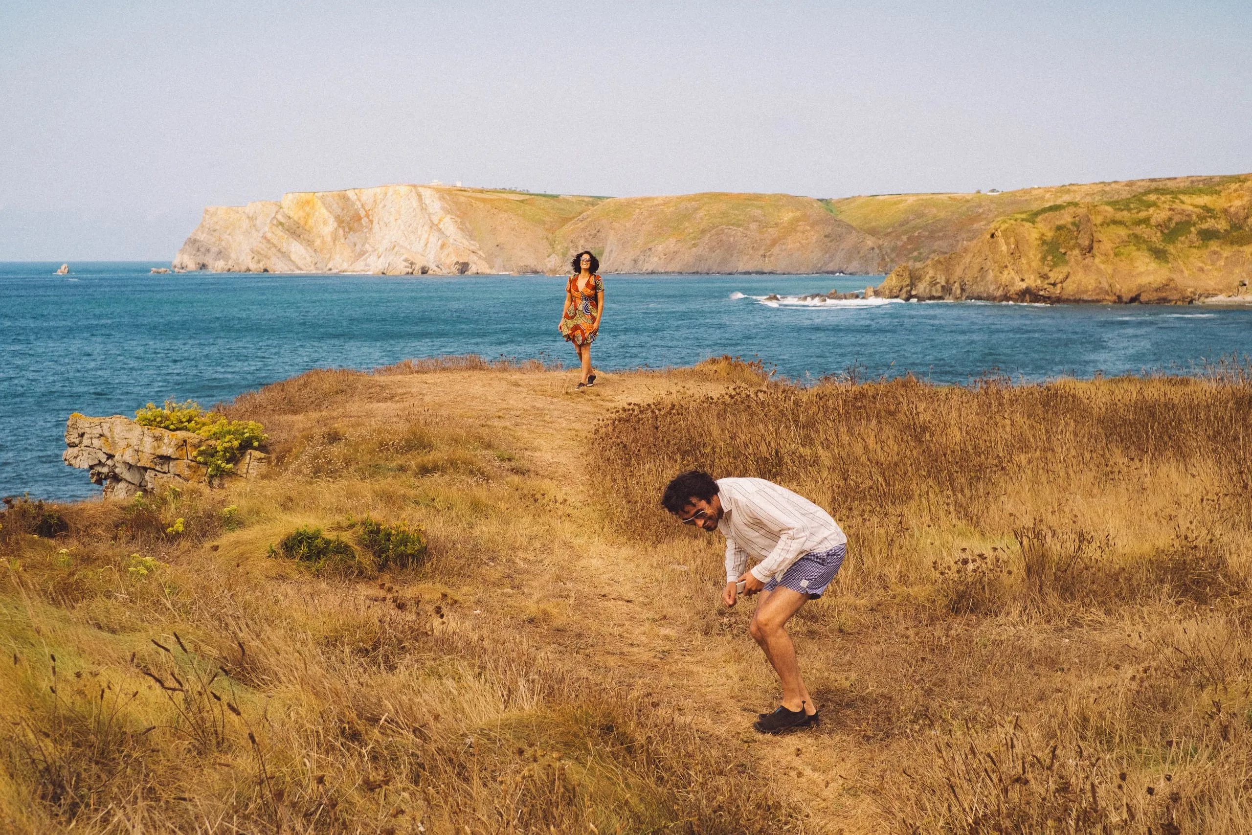 A man and a woman walk a coastal headland path above the sea
