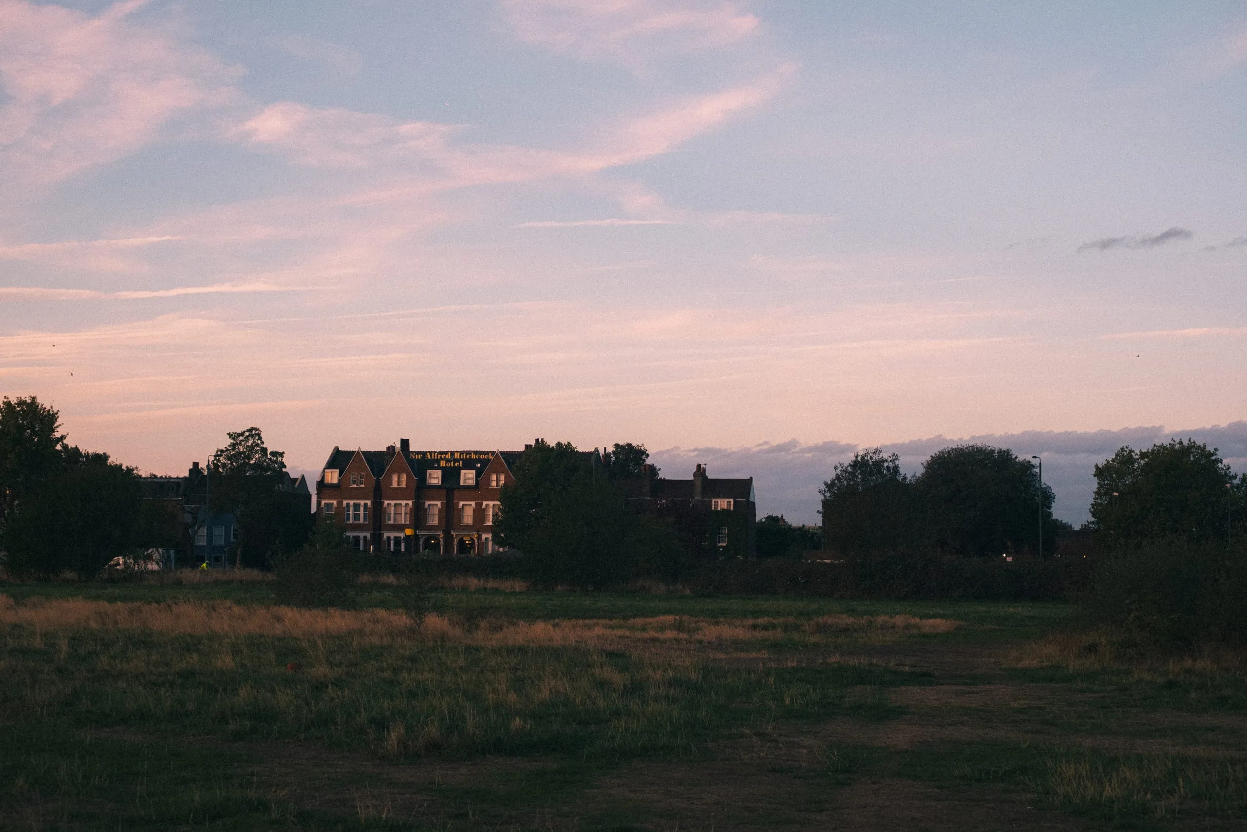 The Sir Alfred Hitchcock Hotel at dusk seen across open ground, Leytonstone